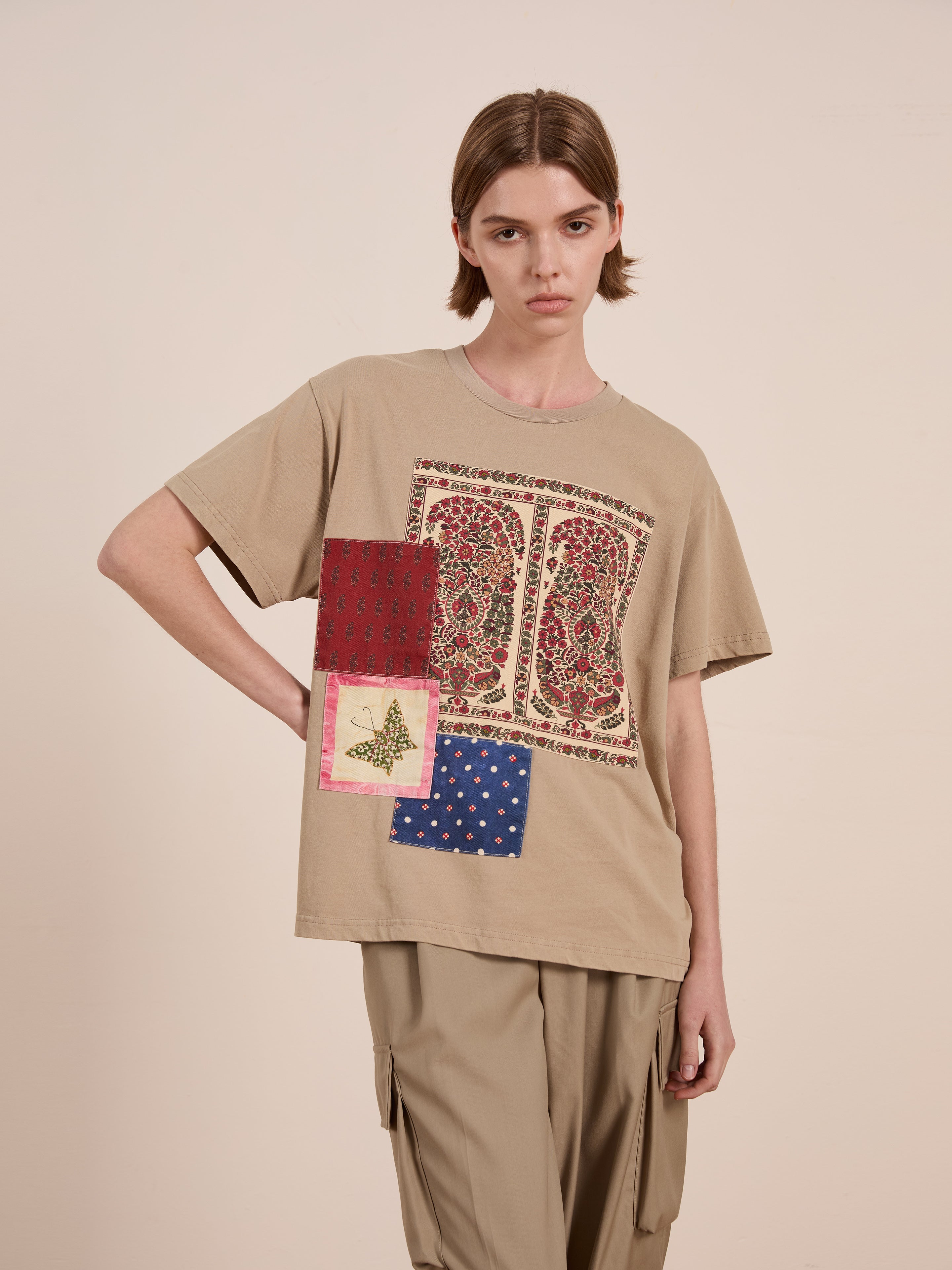 A person in FOUND's beige Patchwork Tee, reminiscent of Kantha embroidery, paired with beige cargo pants, stands against a plain background.