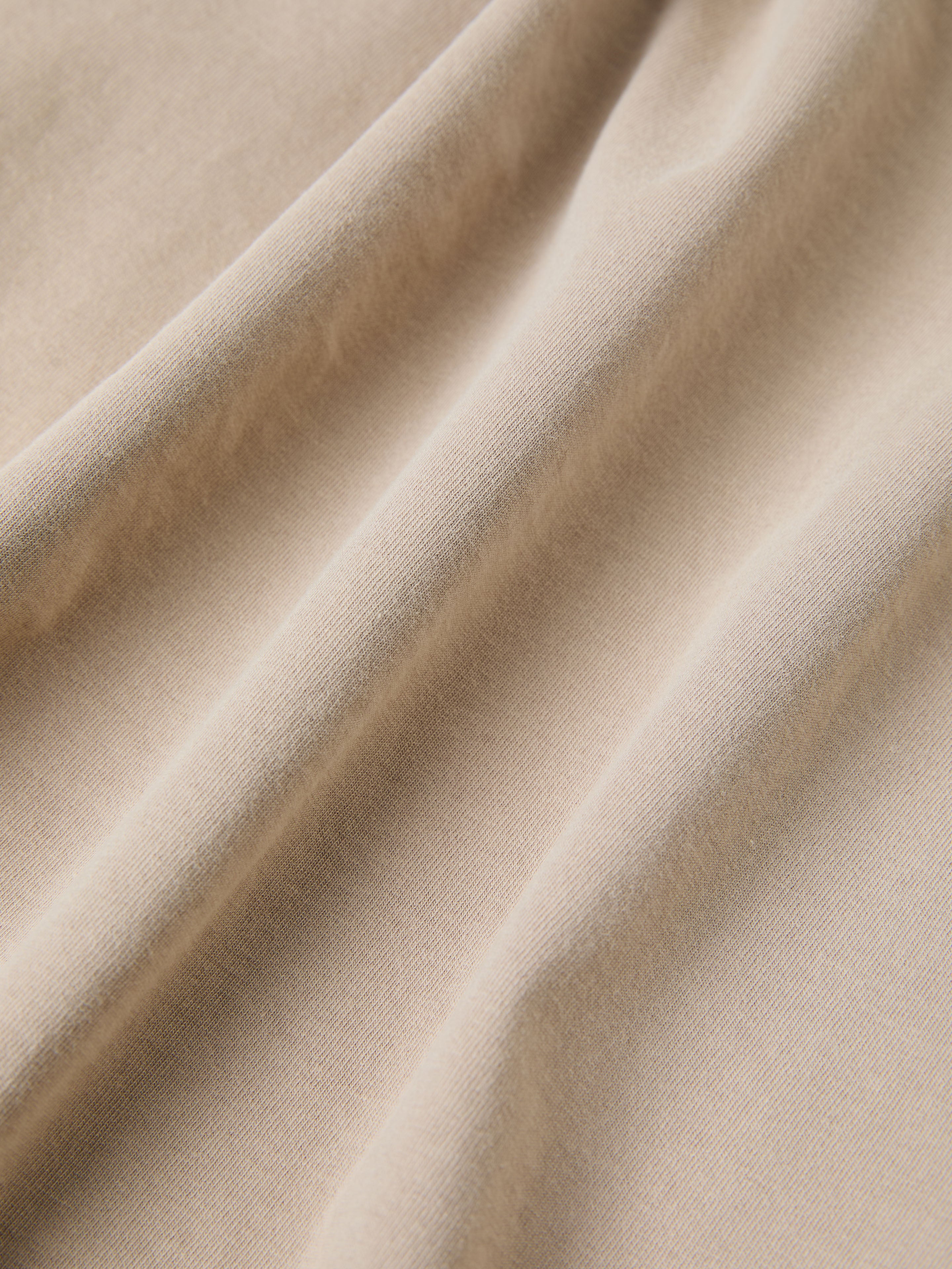 Close-up of the beige fabric in the Patchwork Tee by FOUND, showcasing soft, flowing folds and a smooth texture that evoke intricate South Asian quilt patterns.