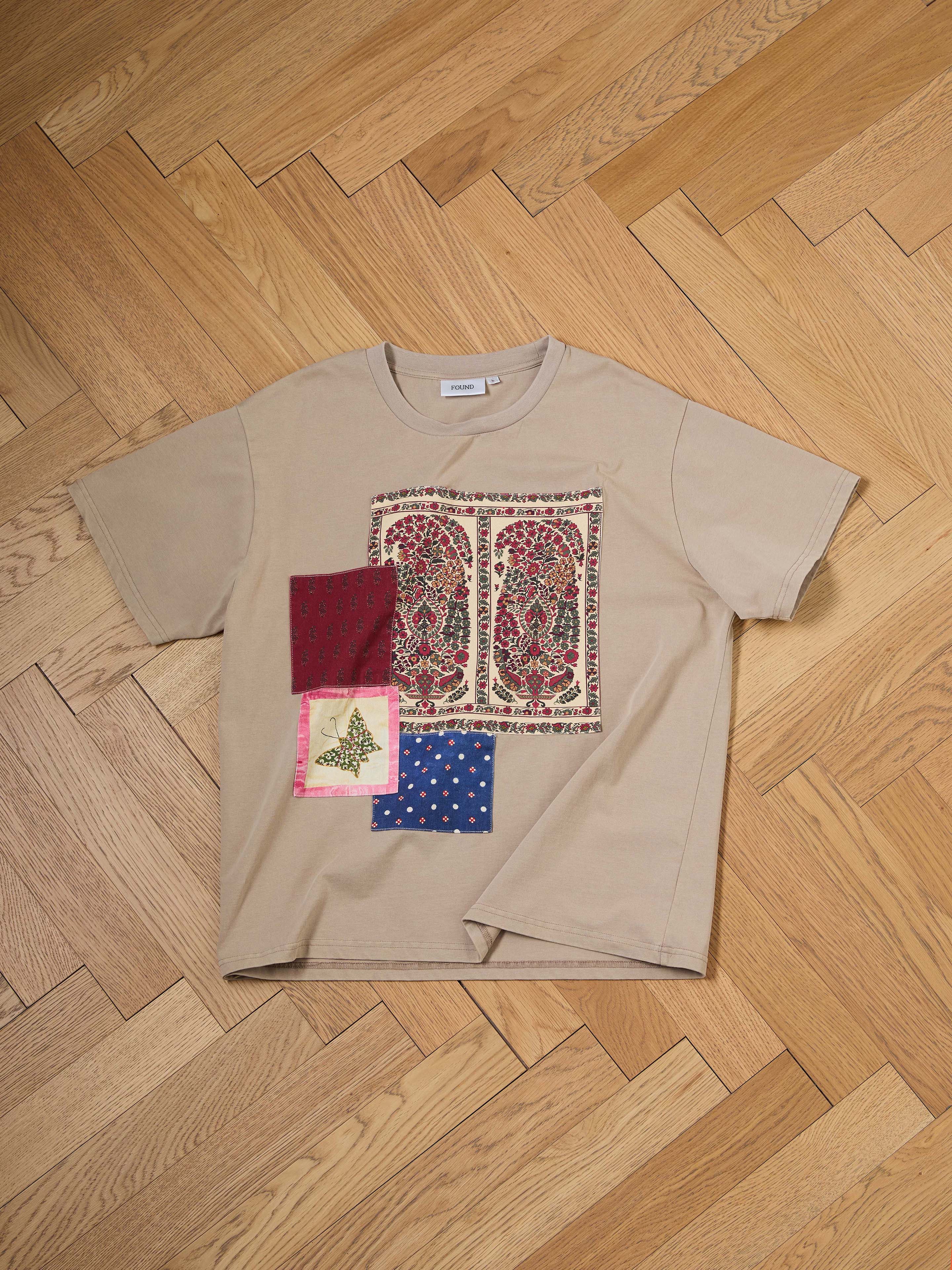 The FOUND Patchwork Tee, in beige with a paisley design, features three fabric patches—one red, one blue, and one butterfly-themed. Evoking South Asian quilts, this unique piece adds vibrant texture and storytelling to your wardrobe.