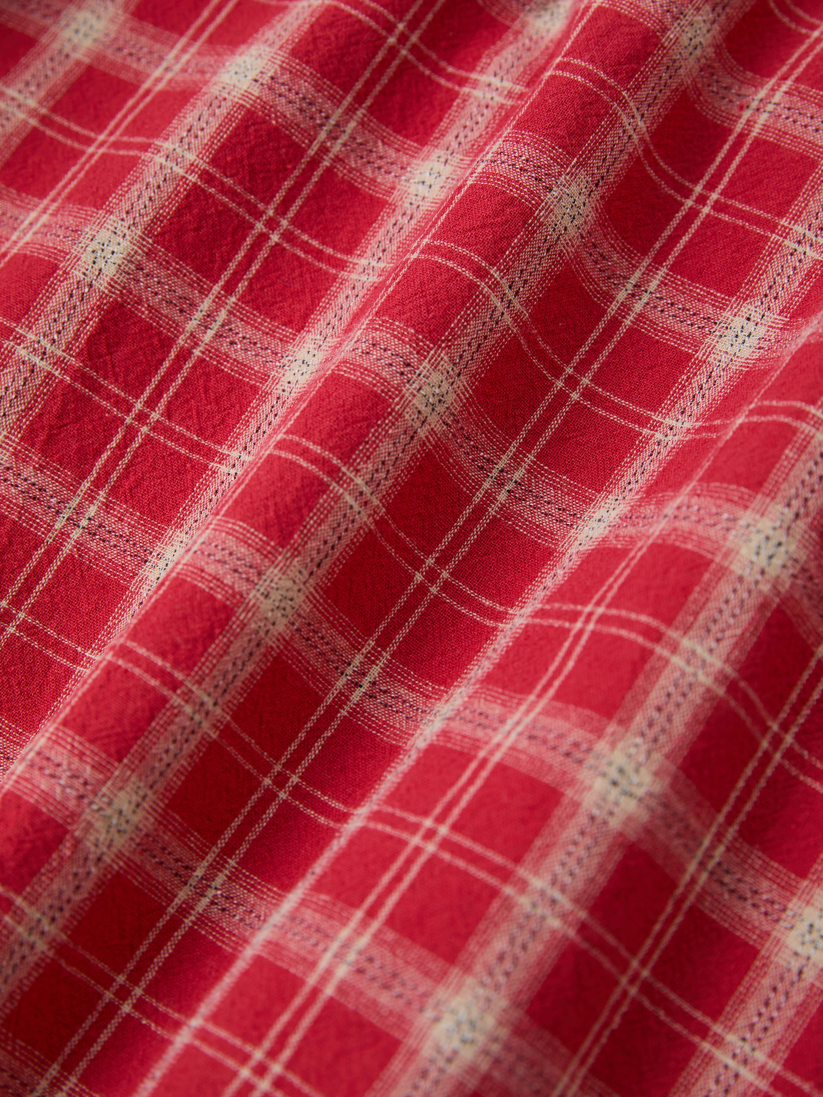 Close-up of red fabric with a white plaid design, echoing the cozy flannel vibe of your cherished FOUND Raw Cut Fringe Plaid Camp Shirt.