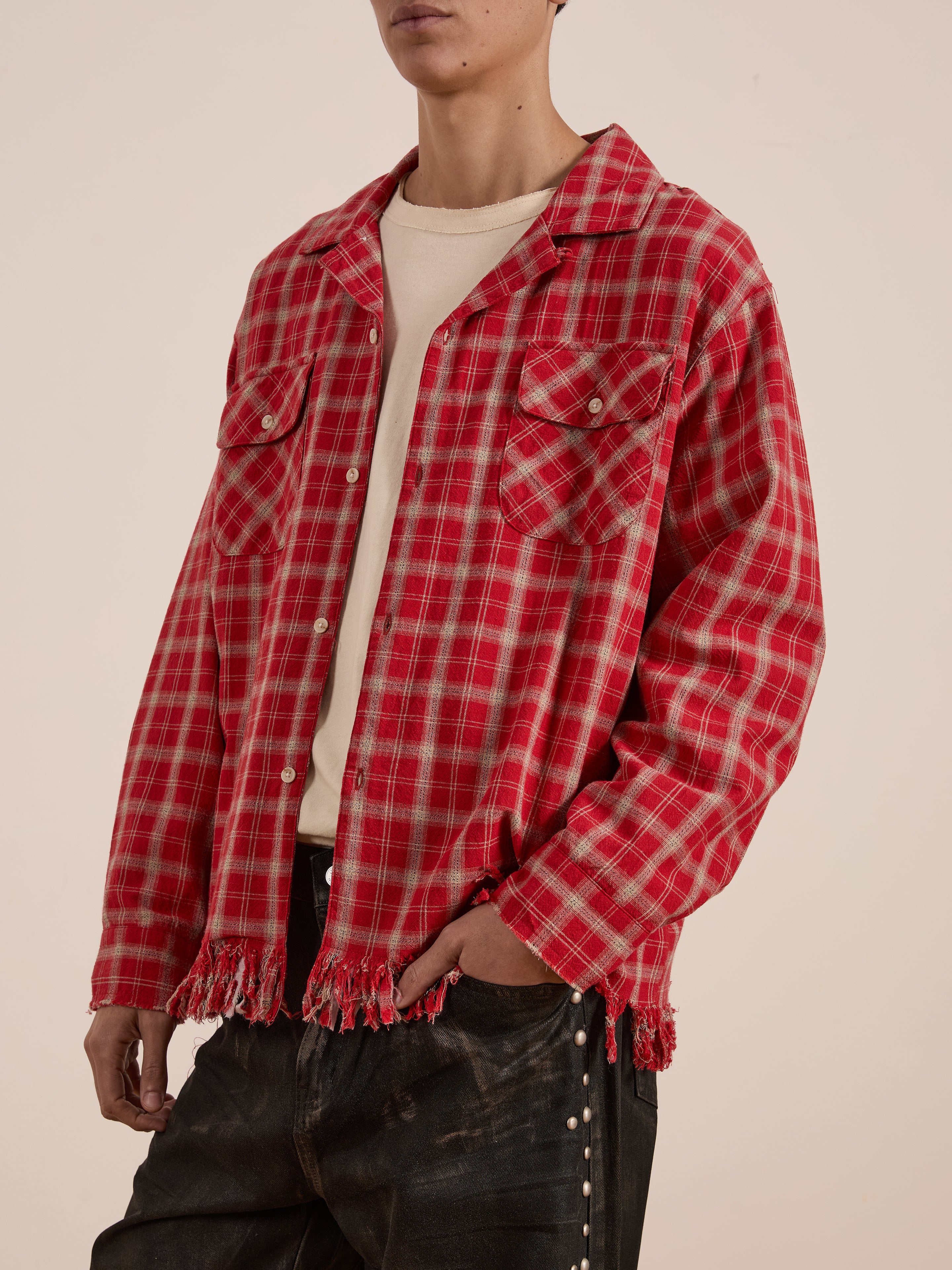 Someone models a red Raw Cut Fringe Plaid Camp Shirt by FOUND, made from soft brushed cotton and featuring a frayed hem, against a plain background, paired effortlessly with dark pants.