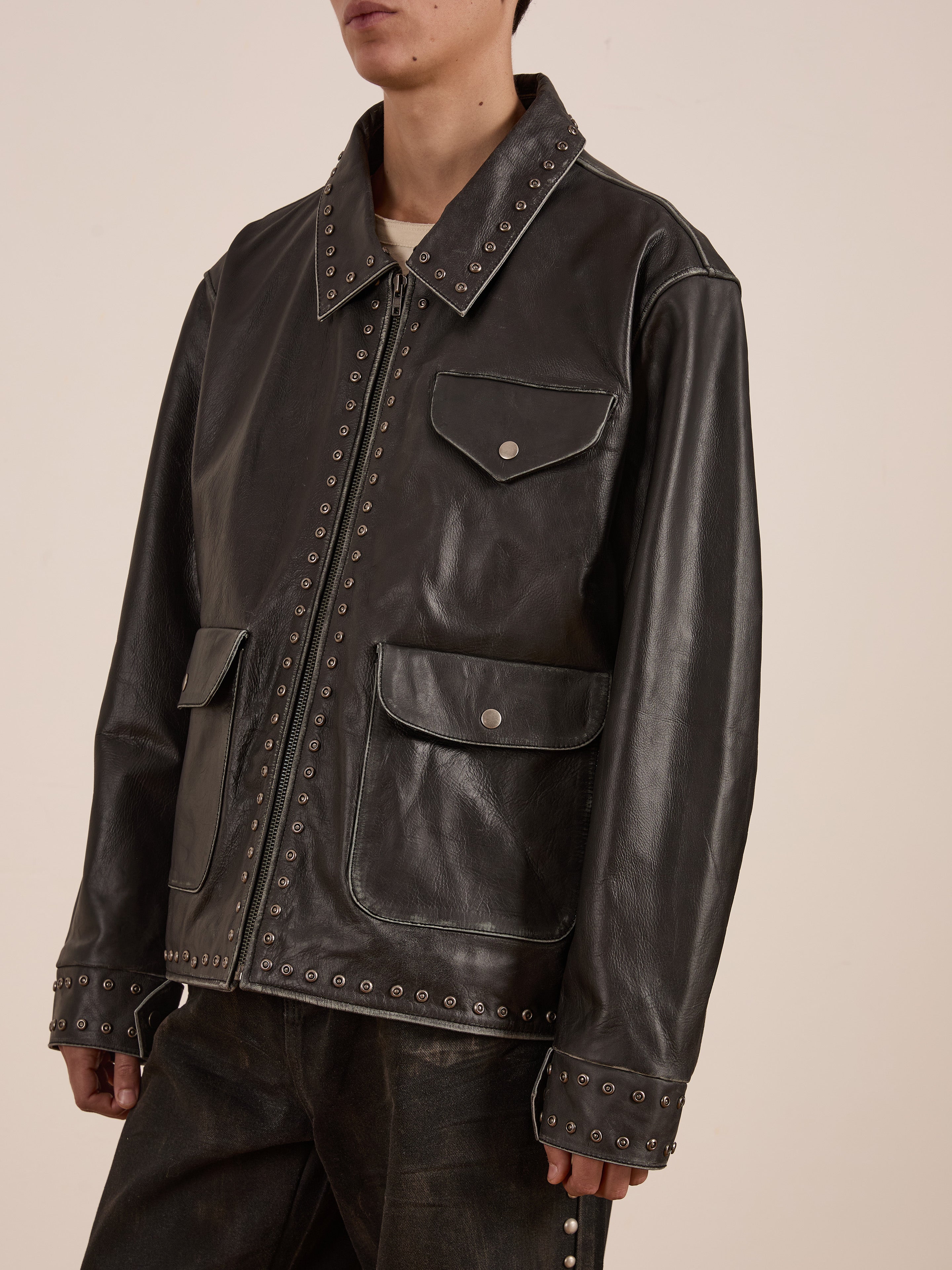 Someone is wearing FOUND's Studded Leather Pocket Jacket, a vintage black leather piece with studded details, paired with matching pants. This unisex jacket includes front pockets and a sleek zip closure.