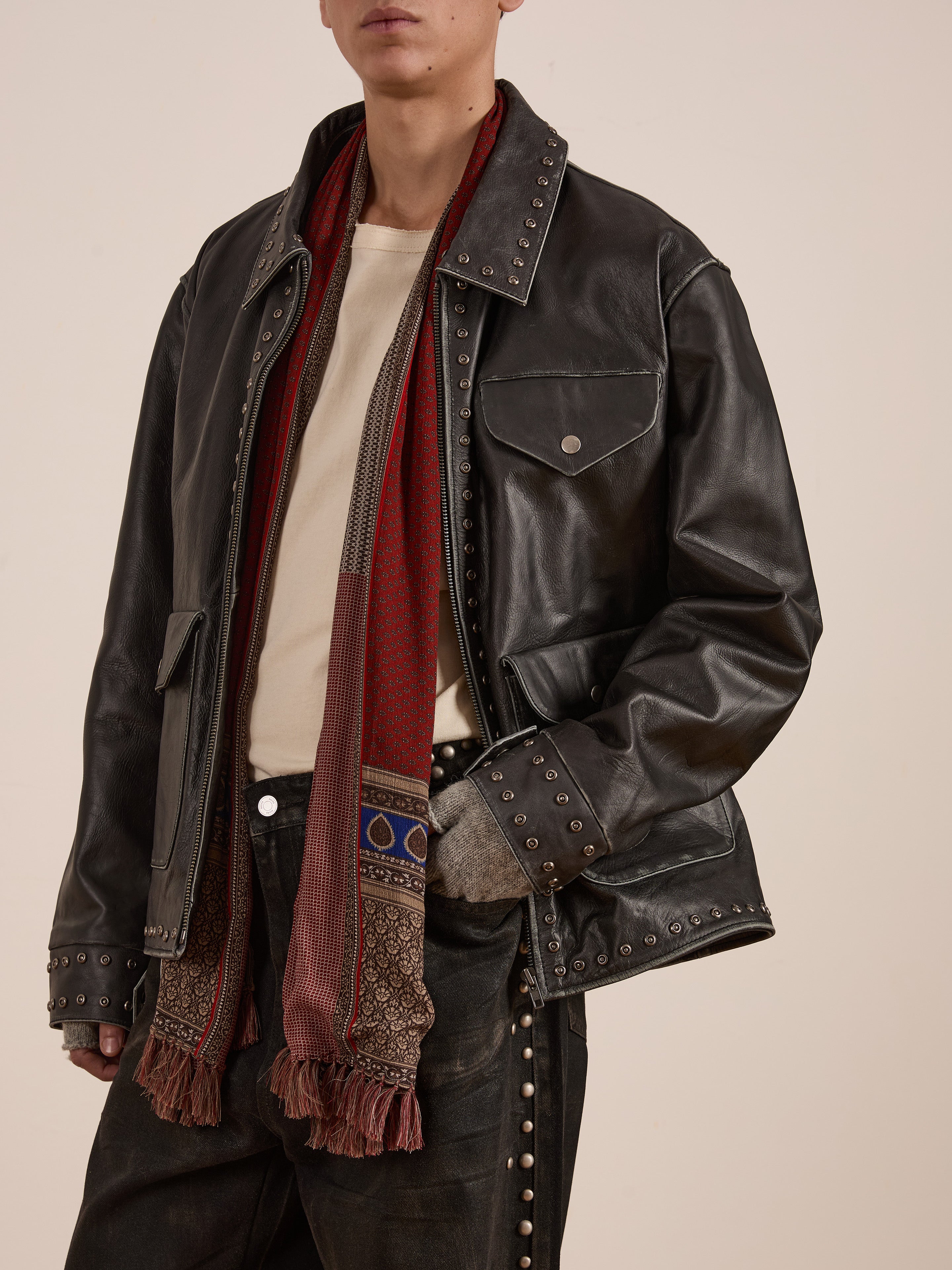 A person wearing the FOUND Studded Leather Pocket Jacket, beautifully paired with a beige shirt and a red patterned scarf.