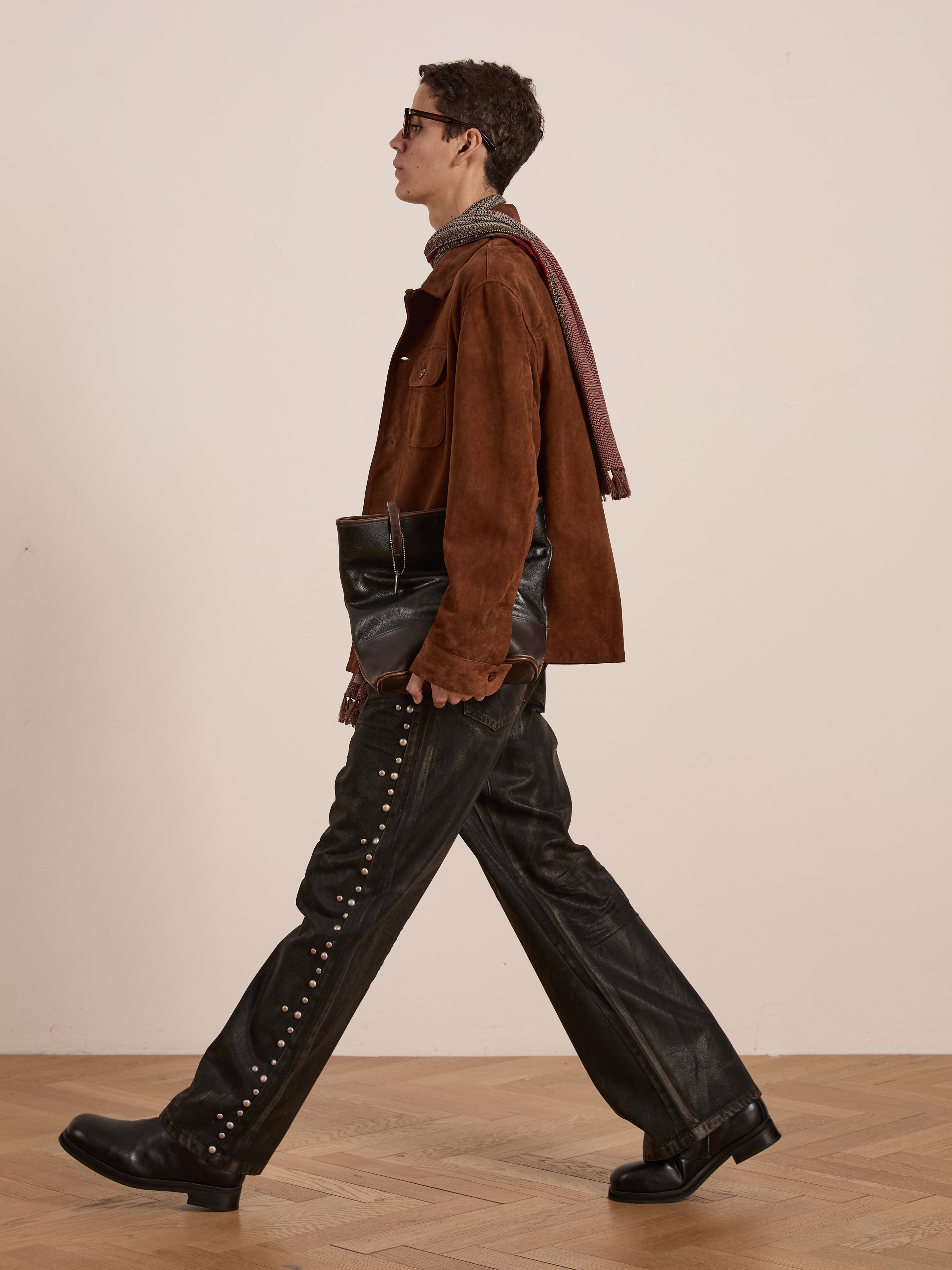 Sporting the FOUND Suede Camp Shirt in a relaxed silhouette, this person pairs it with leather pants studded for style, complemented by boots and a black bag. A pair of sunglasses rounds off the look.