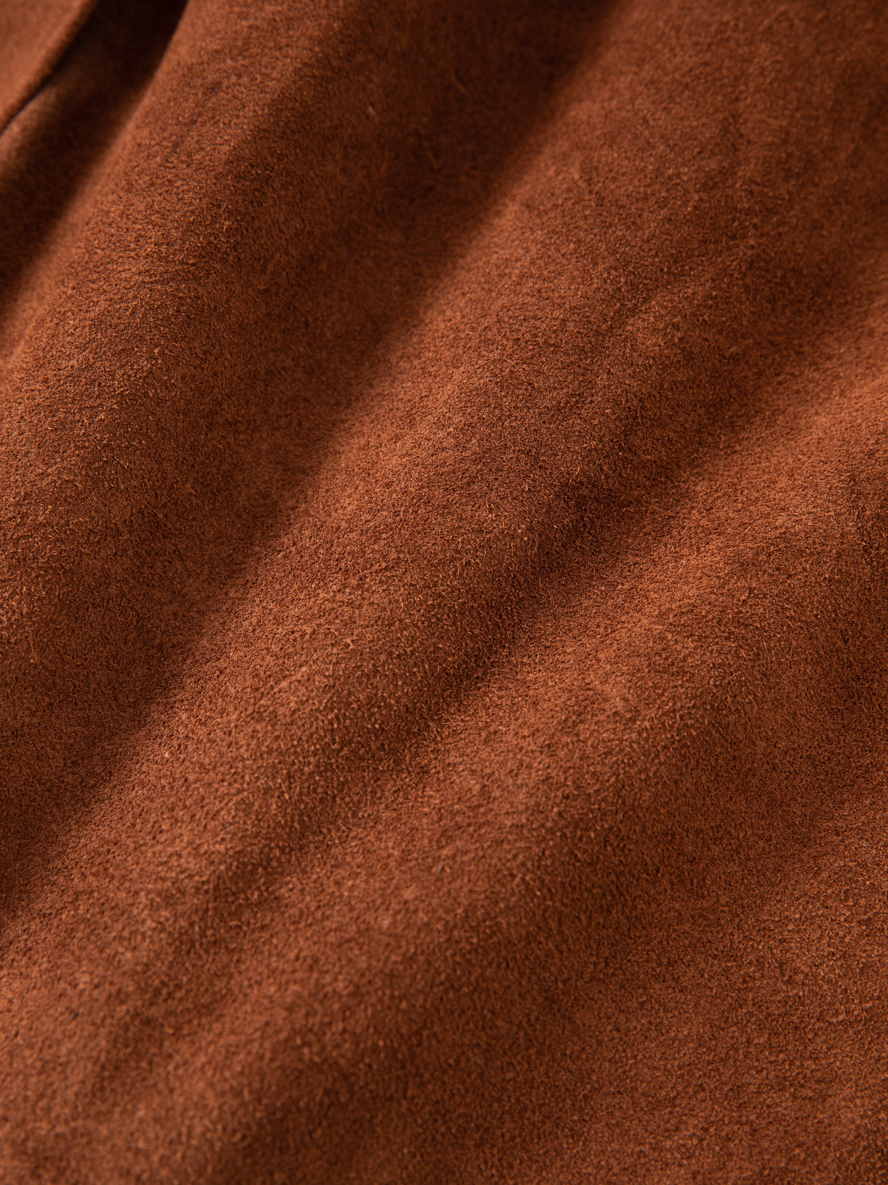 Close-up of the soft, textured surface of FOUND's Suede Leather Trench Coat in brown, reflecting its ethical craftsmanship with slight shadows.