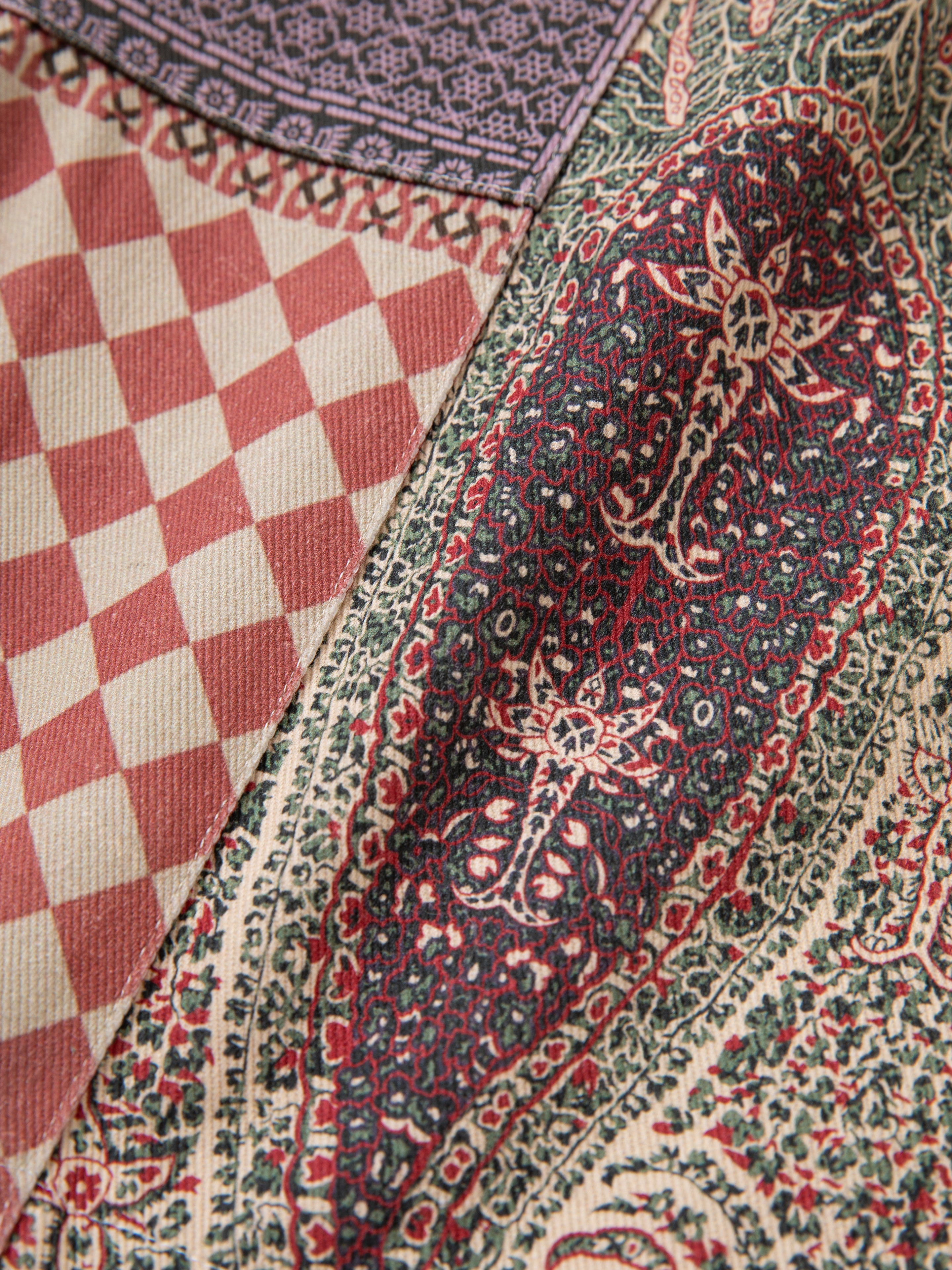 Close-up of the Tapestry Twill Shorts from FOUND, showcasing a mixed-pattern fabric with a red and white checkerboard design on one side and a detailed green, red, and beige paisley pattern on the other.