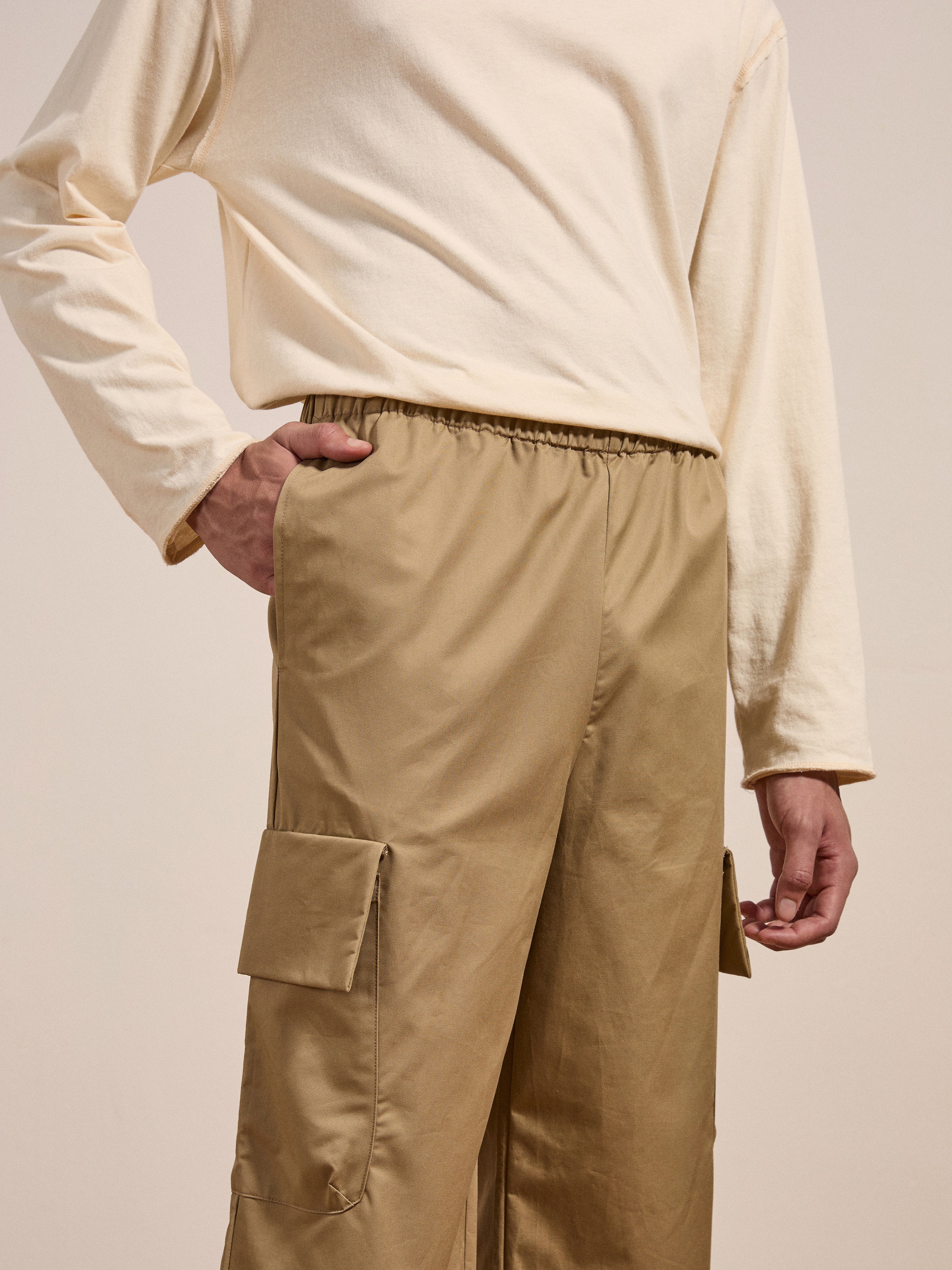 A person in a long-sleeve beige shirt and FOUND's Long Twill Cargo Shorts stands with a hand in their pocket against a neutral background.