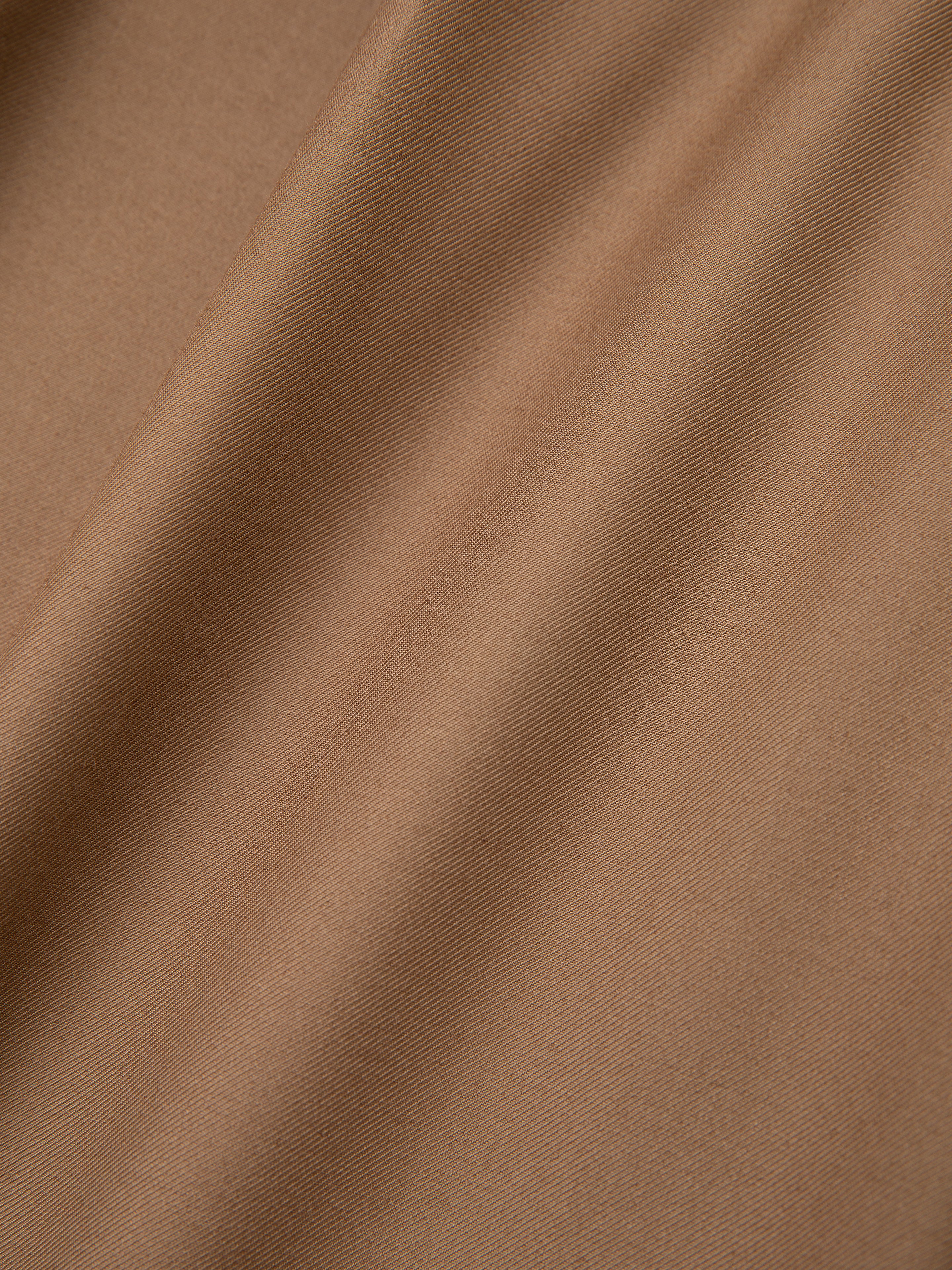 A close-up of the Pleated Trousers from FOUND showcases a smooth brown fabric with diagonal folds, reminiscent of the elegant drape found in high-rise, wide-leg trousers.