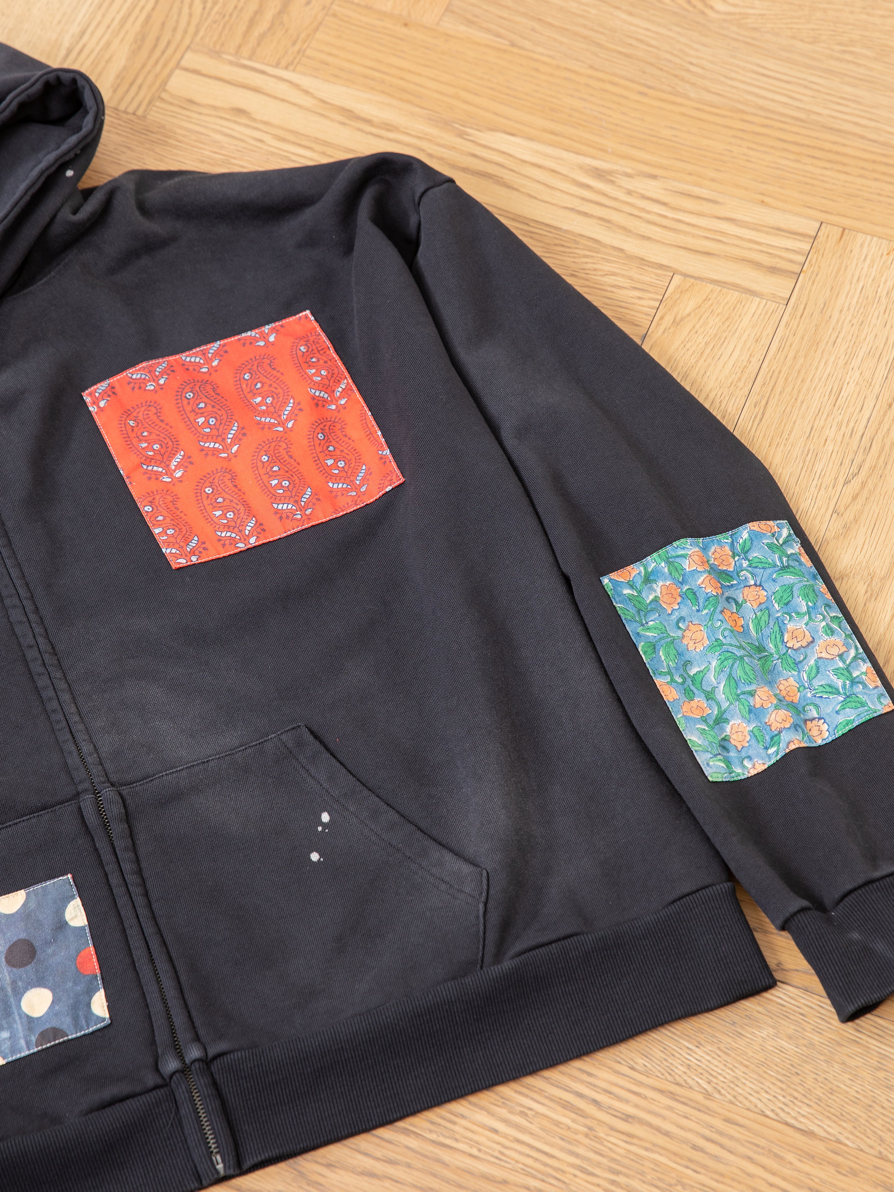 This Tapestry Patchwork Zip Up Hoodie by FOUND features an oversized fit and showcases colorful details, including a red paisley pocket on the chest, a floral pocket on the sleeve, and a polka dot pocket near the hem.