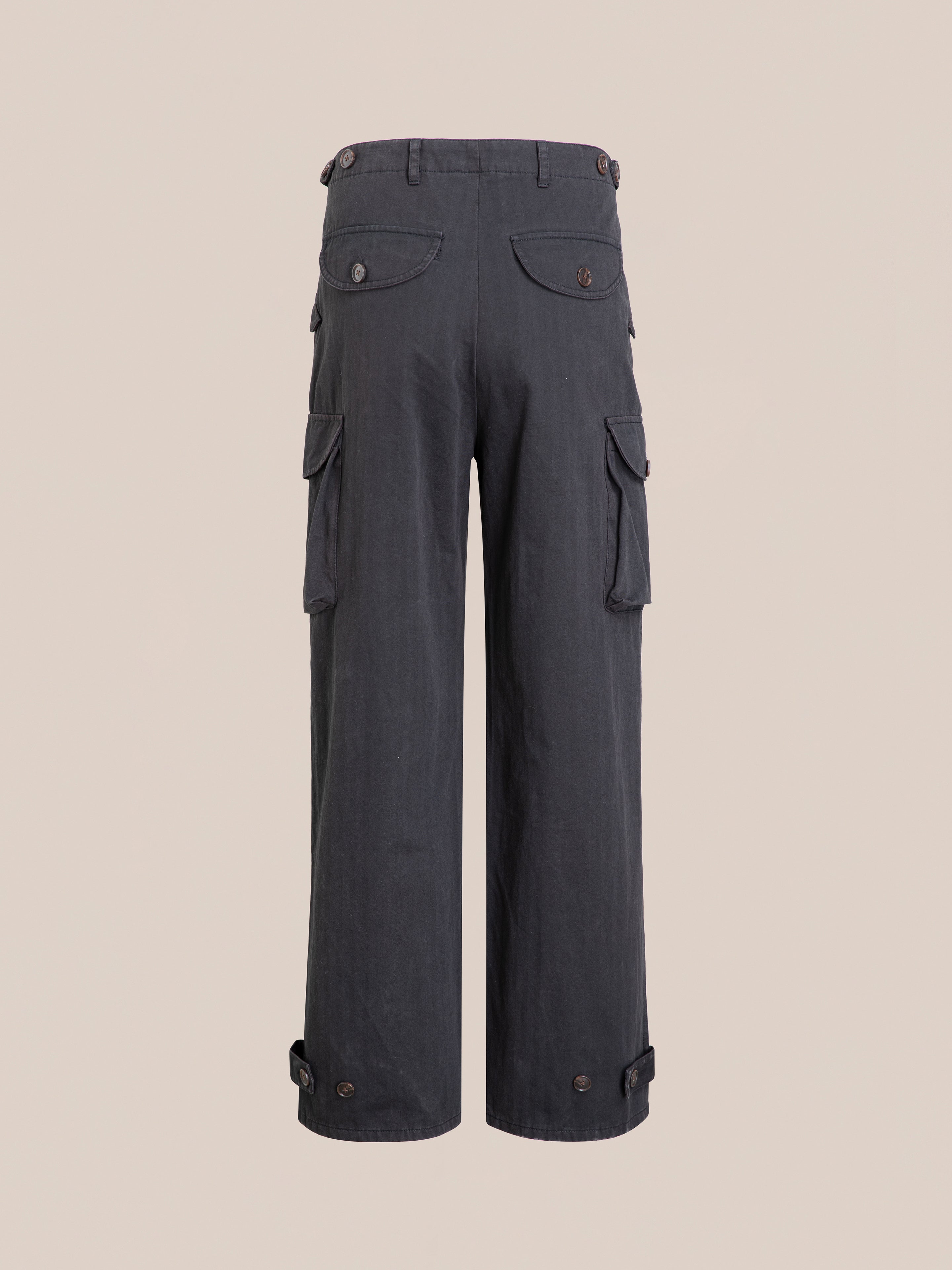 Utility Herringbone Cargo Pants by FOUND feature side pockets, button closures, and adjustable hem straps. Crafted from durable cotton twill for a vintage look in dark gray. Seen from the back against a plain background.