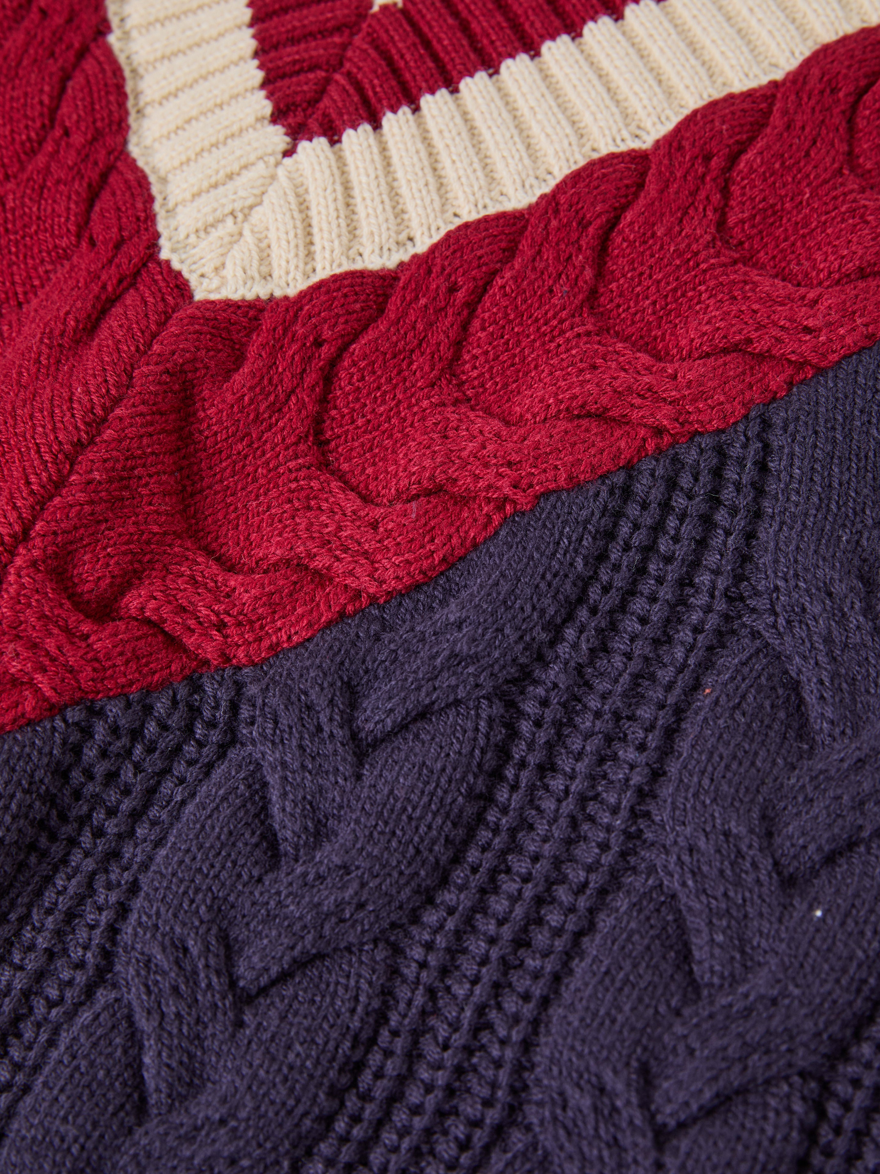 Close-up of FOUND's V-Neck Cricket Sweater showcasing detailed cable knit patterns in red, cream, and navy.