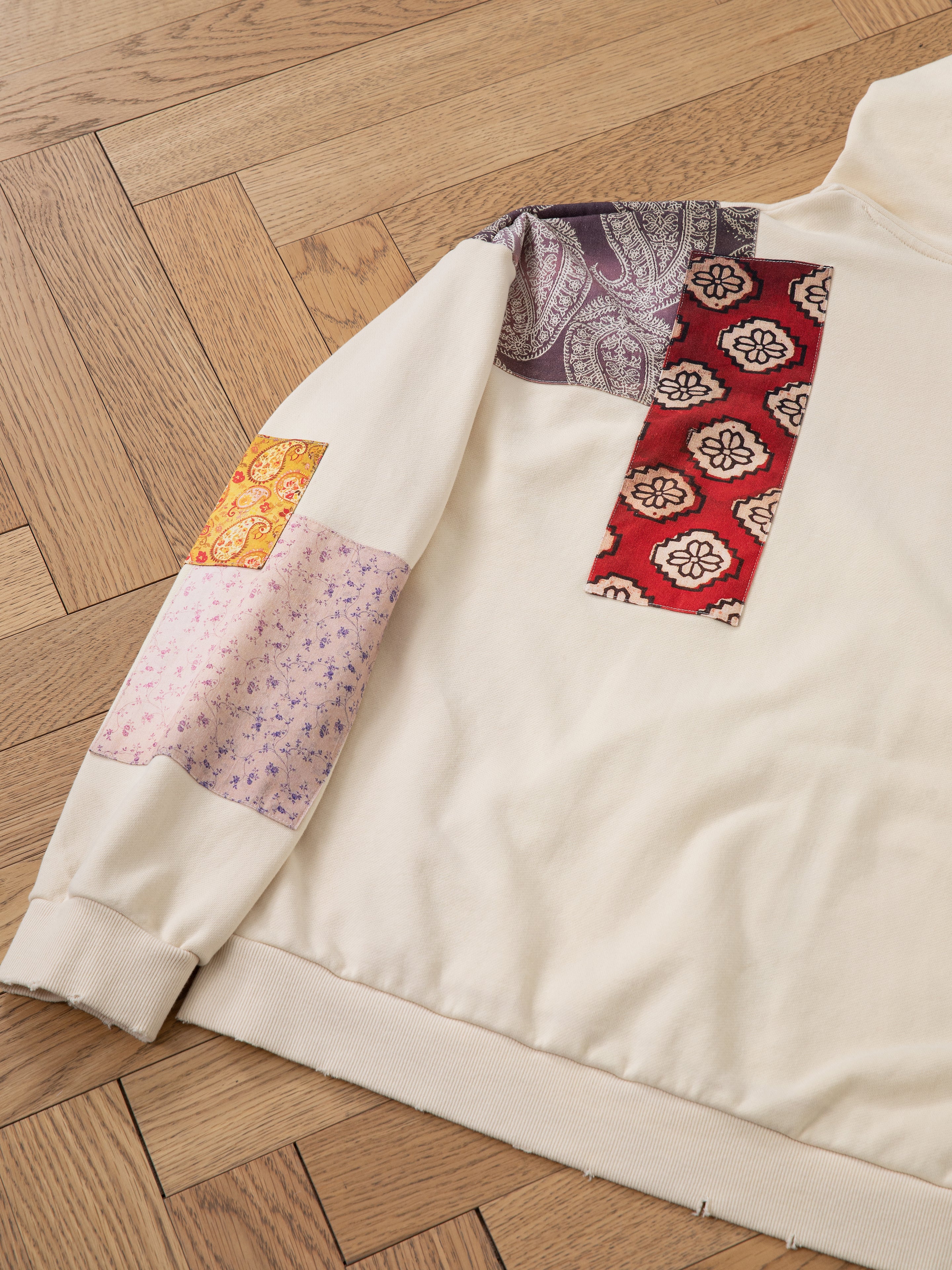 Close-up of the Tapestry Patchwork Zip Up Hoodie by FOUND, showcasing vibrant South Asian tapestry patterns on the back and sleeve, lying on a wooden floor.