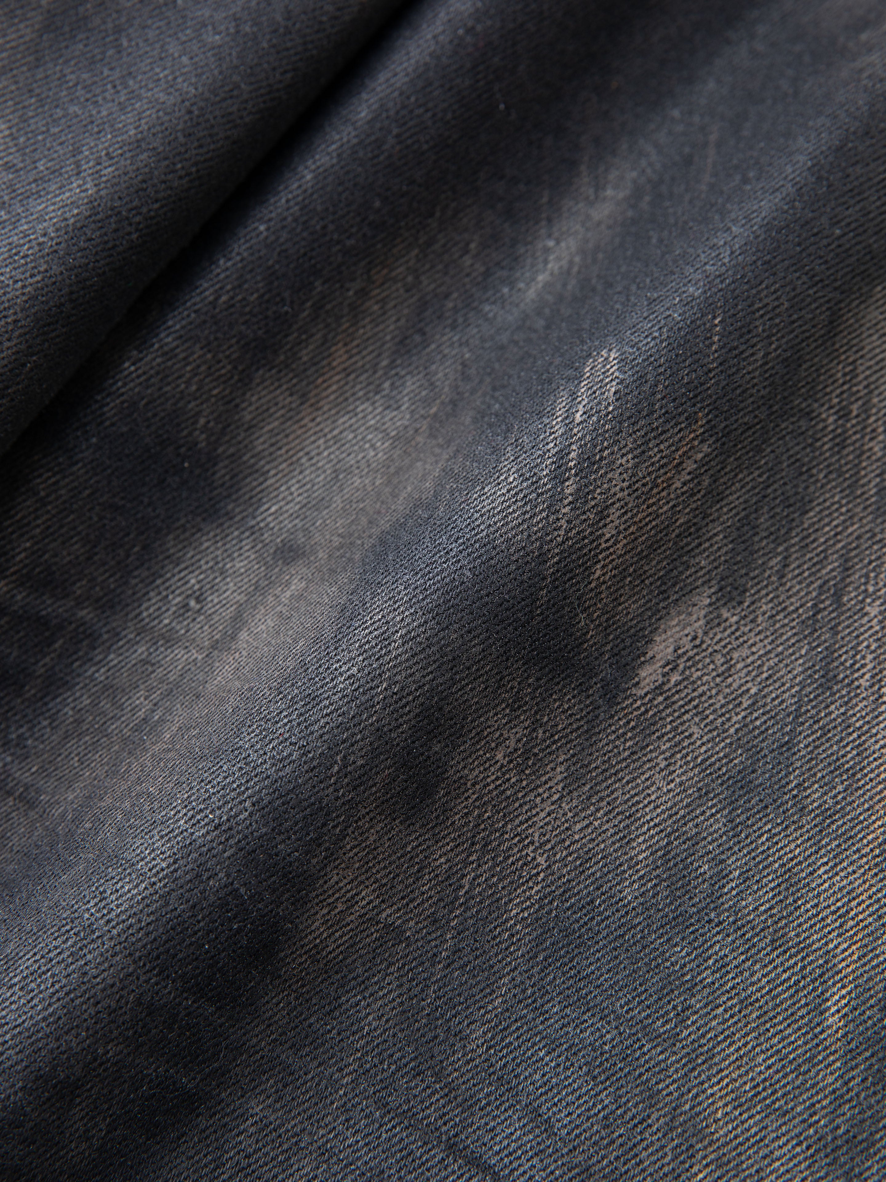 Close-up of faded, distressed black denim fabric from FOUND's Waxed Studded Jeans, featuring a textured, worn appearance that highlights vintage craftsmanship.