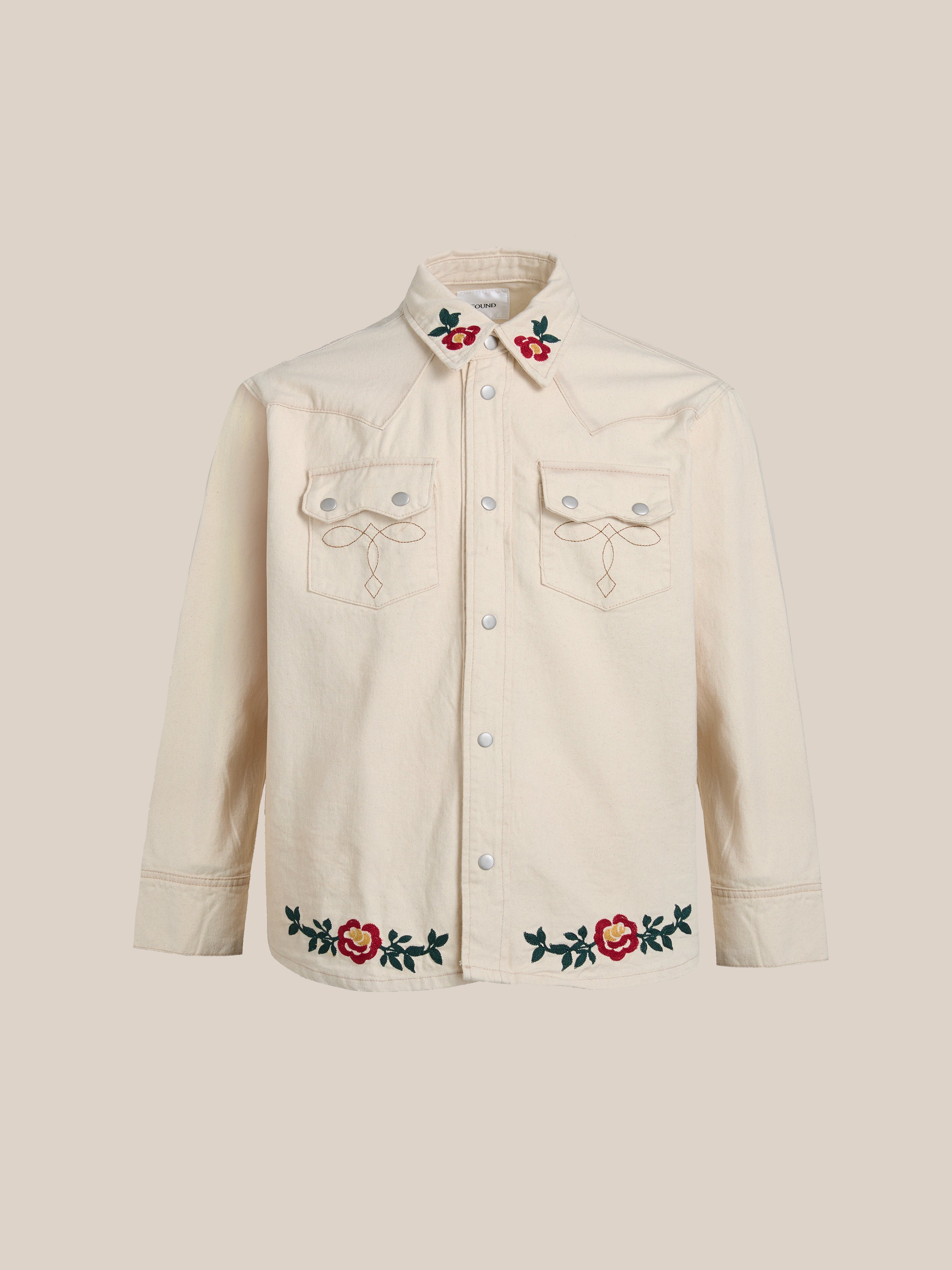 The Western Floral Denim Shirt by FOUND features a cream-colored design with floral chainstitch embroidery on the collar, chest pockets, and hem. It includes a button-up front and long sleeves for an elegant look.