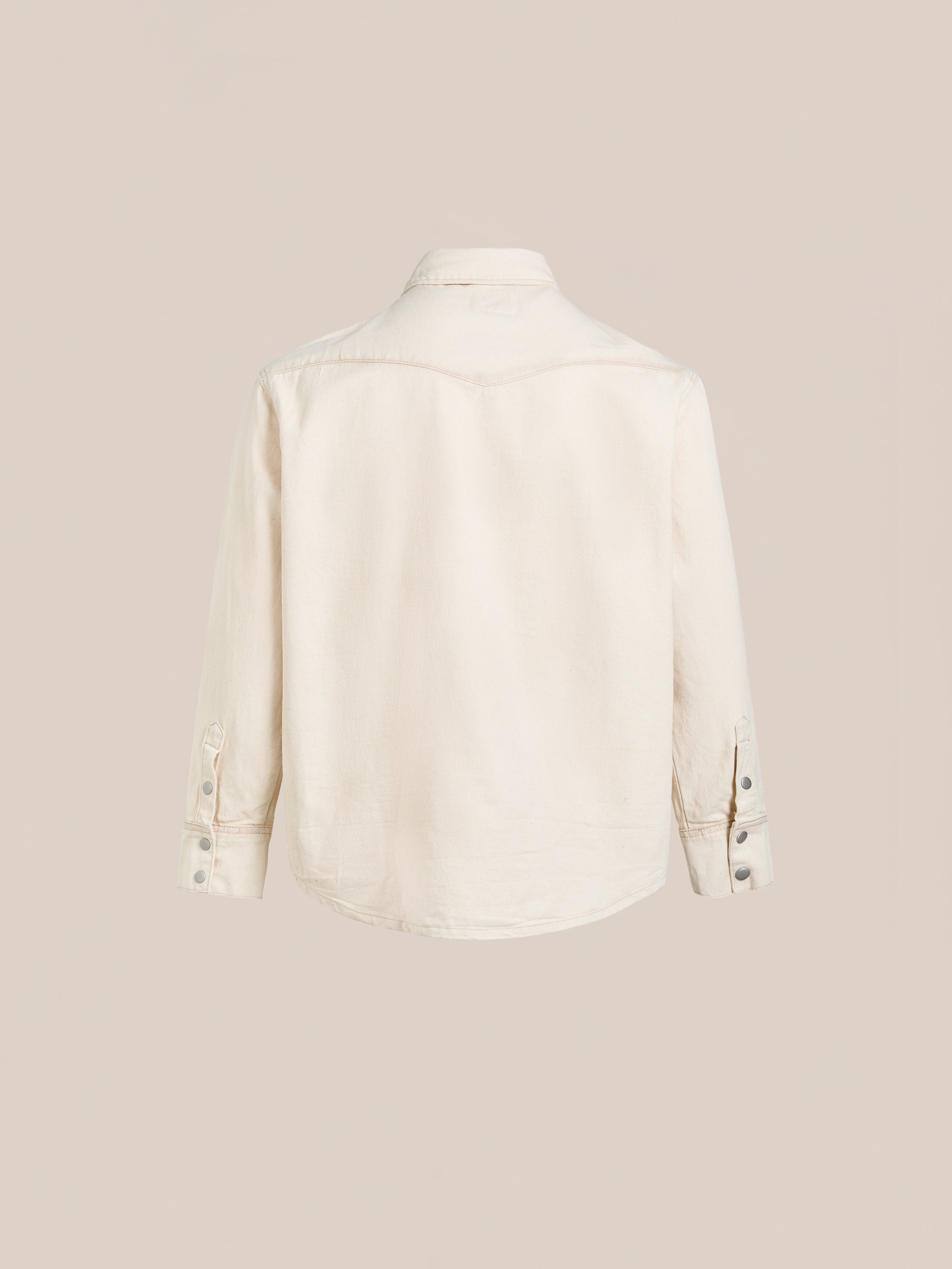 Back view of the Western Floral Denim Shirt by FOUND, featuring long sleeves, buttoned cuffs, and detailed floral chainstitch embroidery on a cream-colored fabric against a plain background.