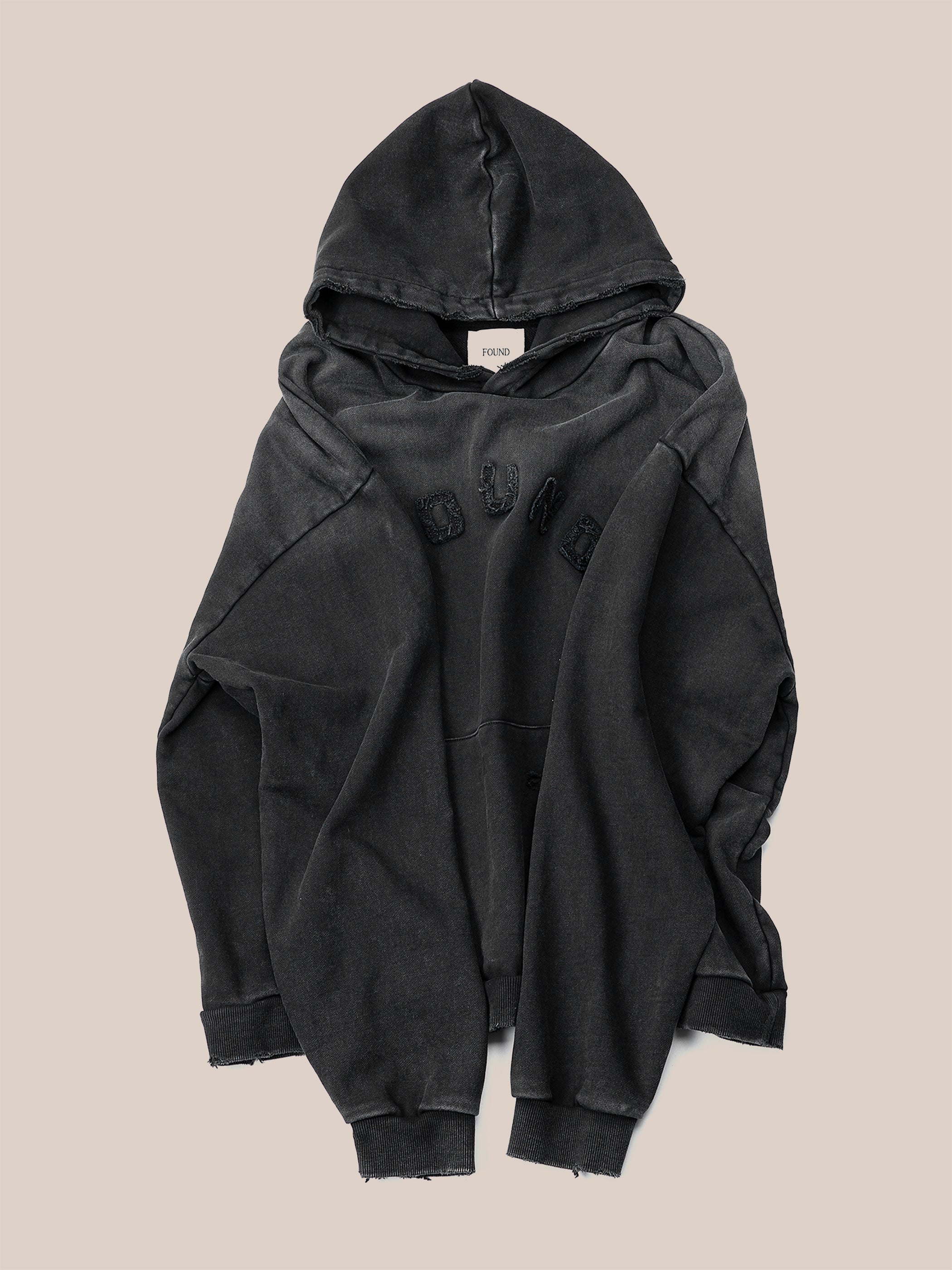 A vintage black Logo Patch Hoodie from FOUND, featuring frayed edges and a subtle distressed logo on the chest, crafted from soft French terry cotton, is laid flat against a neutral background.