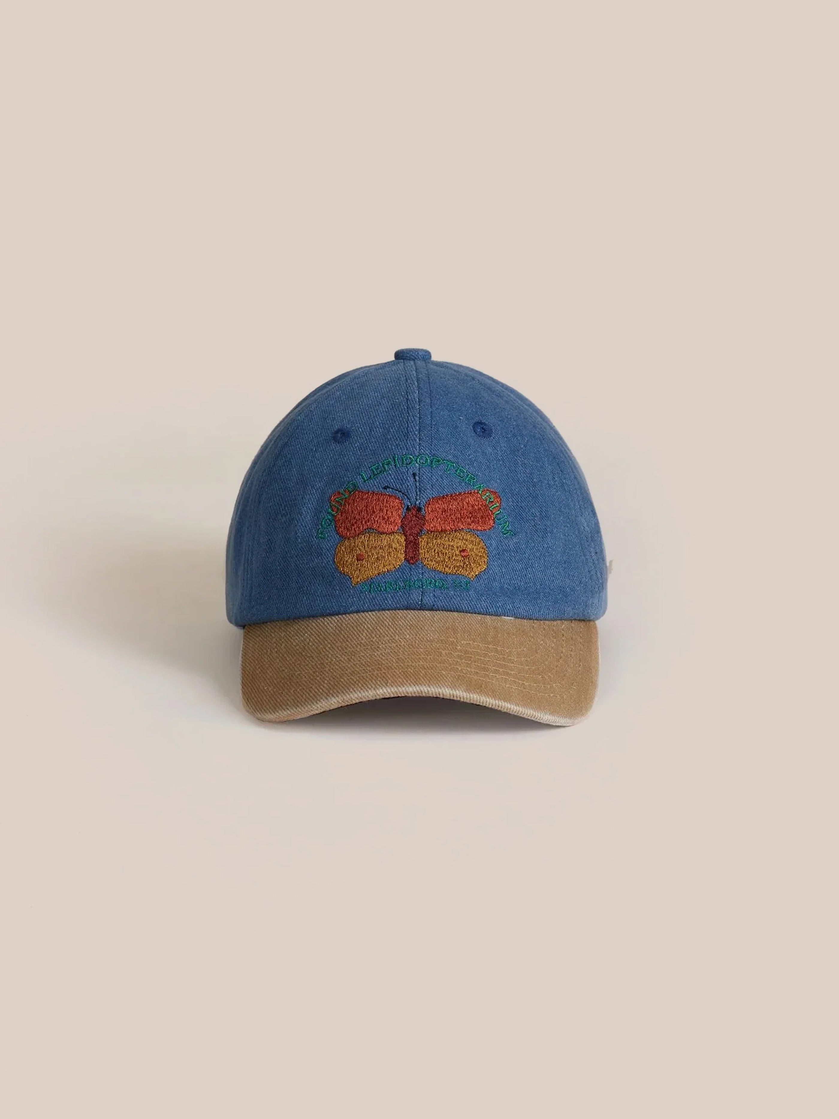 The Found Butterfly House Denim Cap features a beautiful butterfly embroidery on the front, enhanced by a tan corduroy brim that adds a rustic touch.