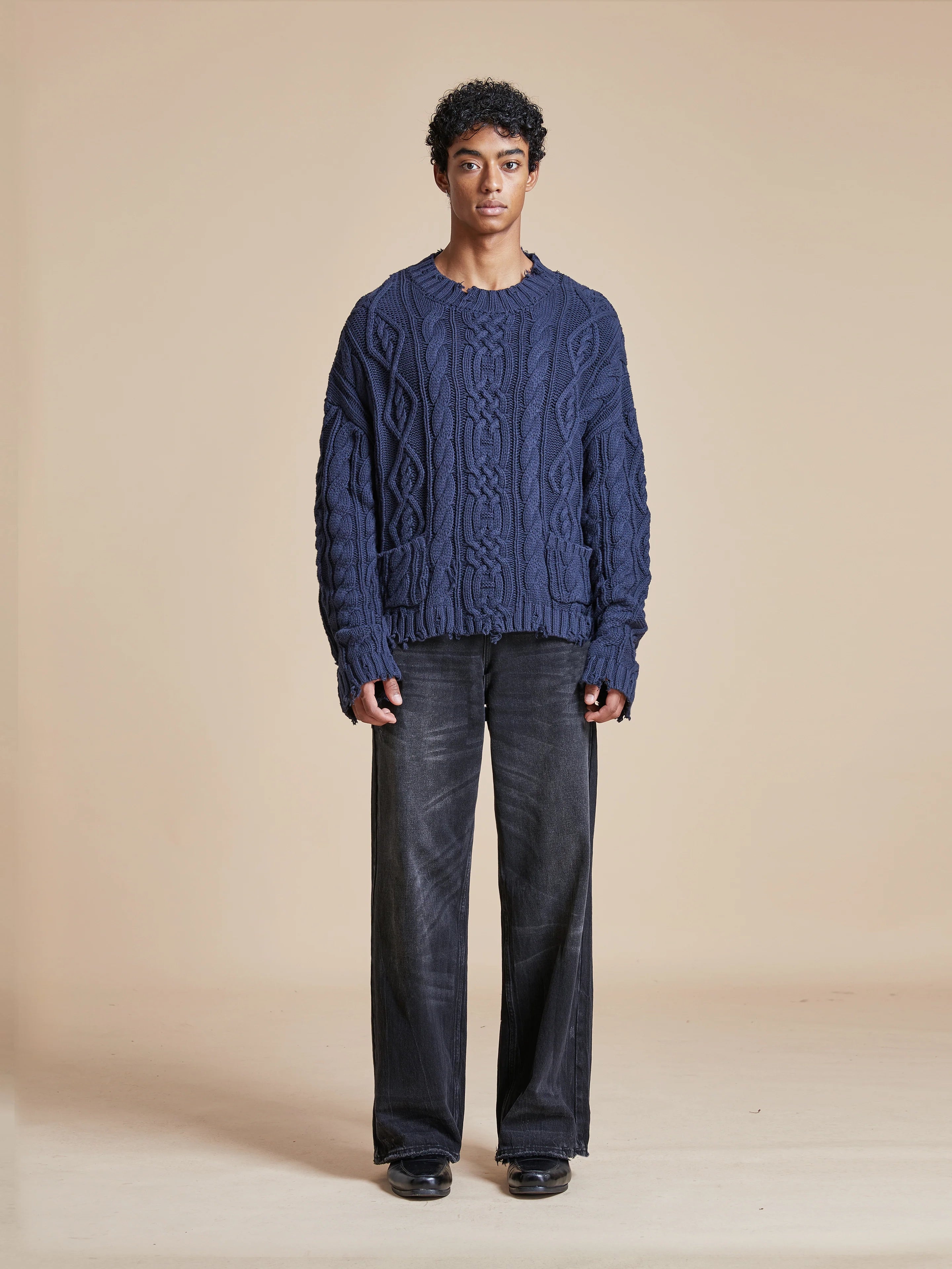 A man donning an Astral Distressed Cable Knit Sweater from Found in softness and warmth, paired with black pants.