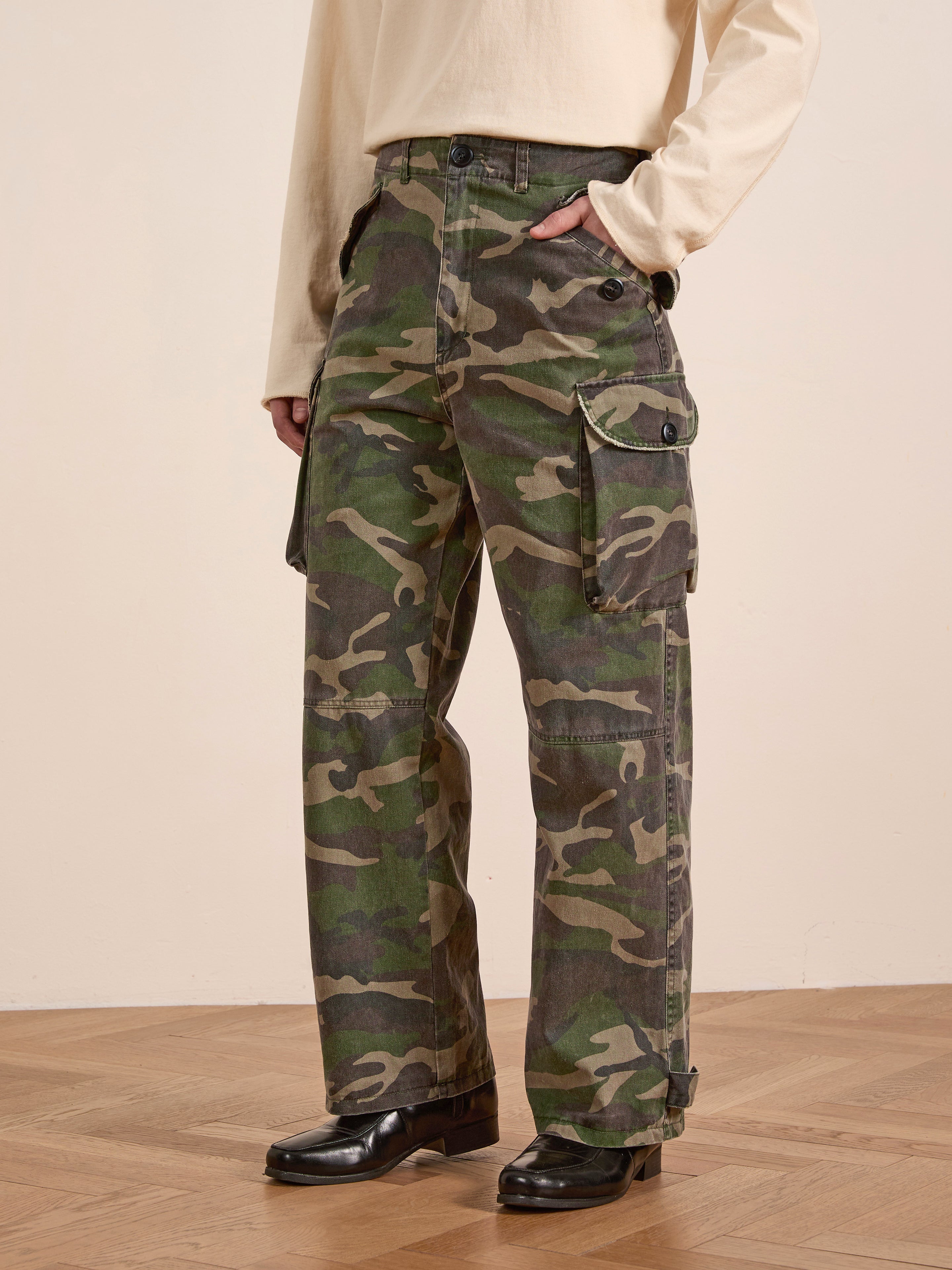 On a wooden floor, someone wears FOUND's Camouflage Twill Utility Cargo Pants in midweight cotton twill with a light long-sleeve shirt.