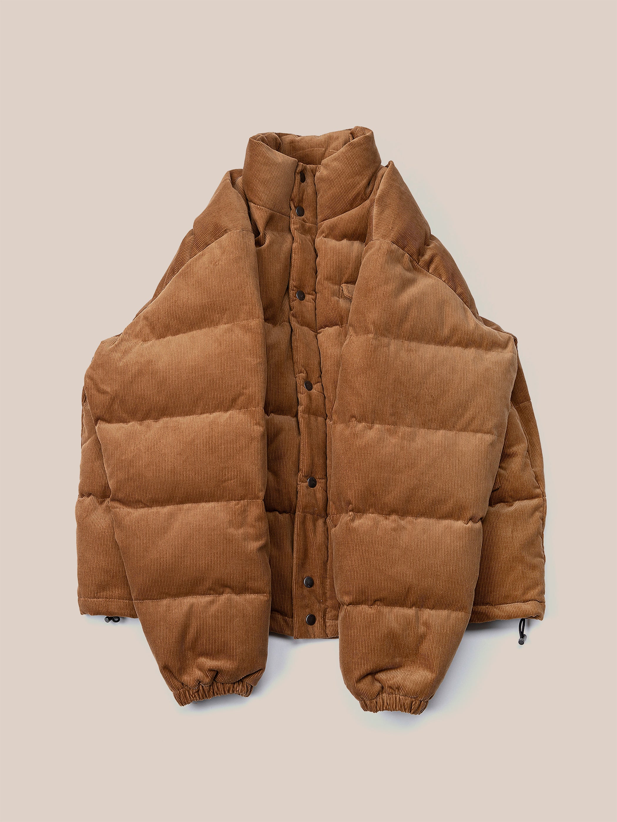 A cozy tan Corduroy Puffer Jacket by FOUND, featuring a button-up front and elastic cuffs, is displayed flat on a neutral backdrop to highlight its relaxed fit.