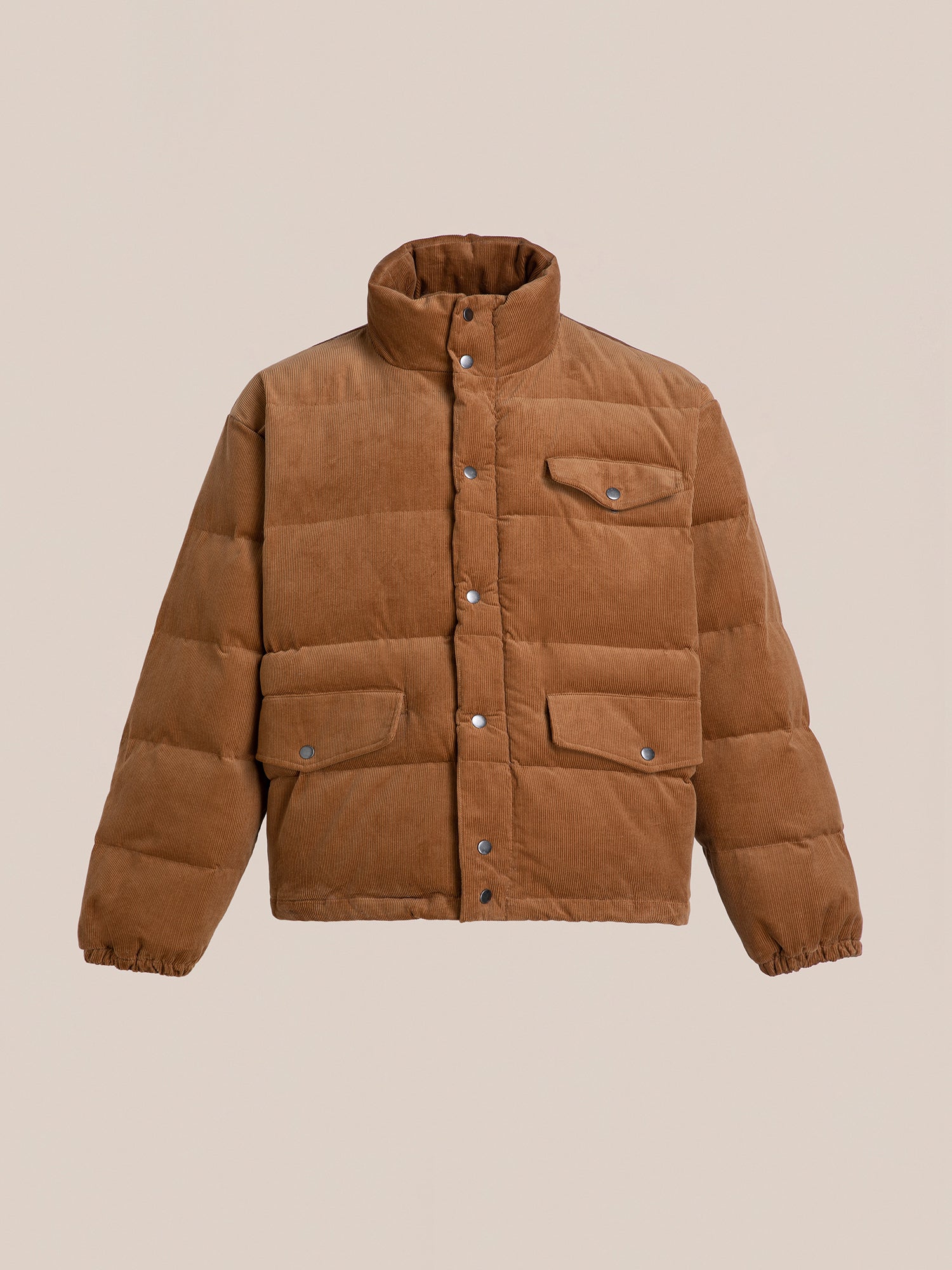 The Corduroy Puffer Jacket by FOUND, in a warm tan shade, boasts a high collar and front pockets, making it ideal against a neutral background.