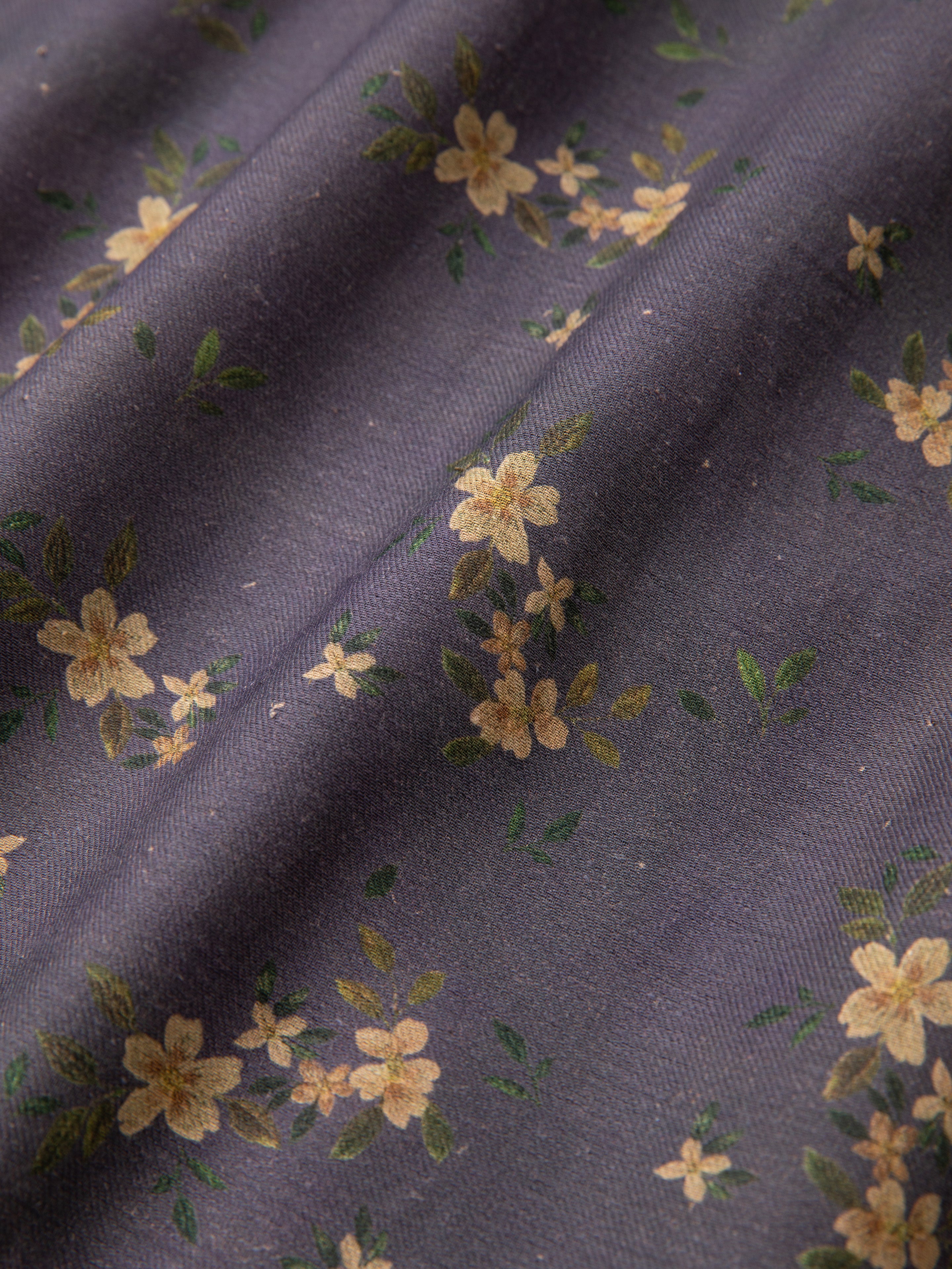 Close-up of a dark purple fabric with a small yellow flower and green leaf pattern, reminiscent of the classic appeal you'd expect from the Dusty LS Camp Shirt by Found. The fabric appears to be slightly wrinkled, adding to its timeless charm.