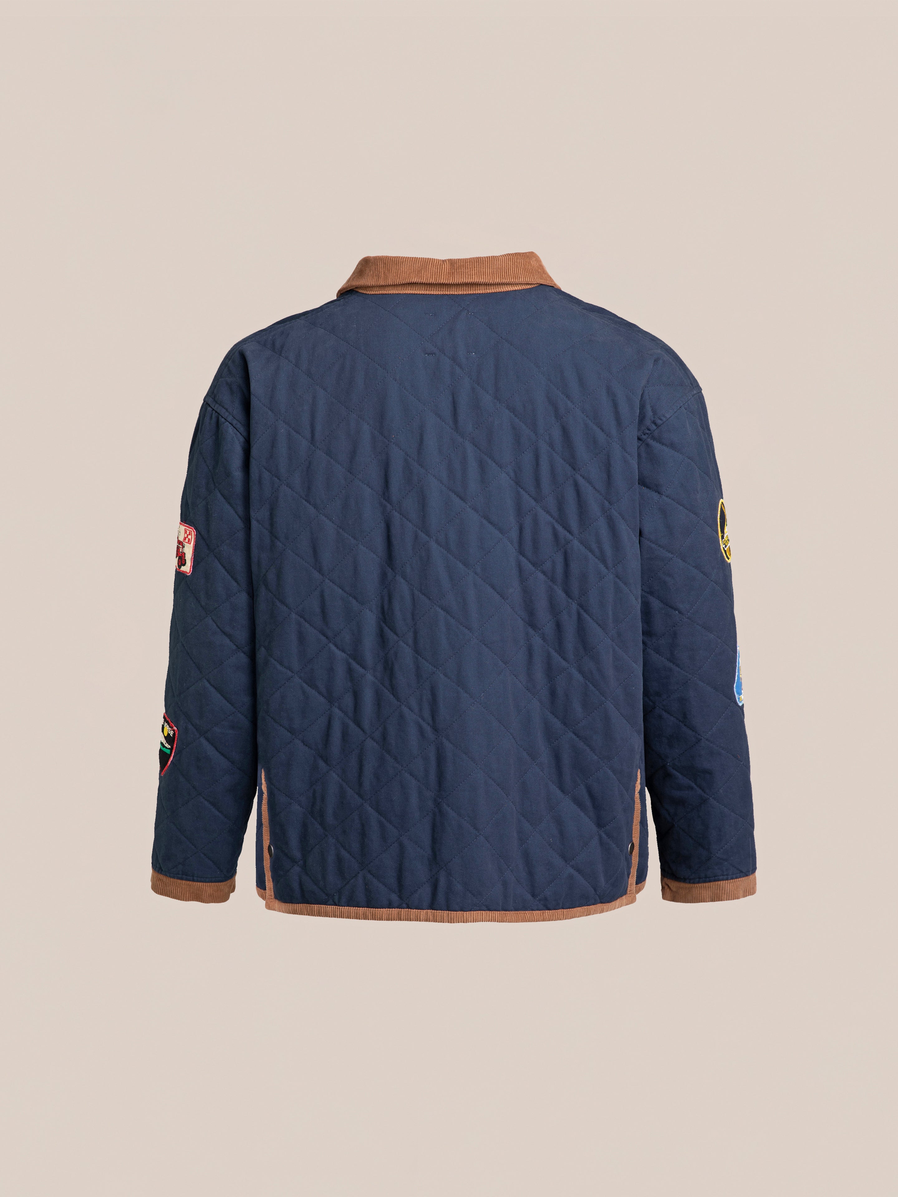 Back view of the FOUND Farmstead Quilt Patch Jacket, featuring a quilted navy design with a brown collar and various patches on the sleeves, reminiscent of vintage hunting competition jackets, displayed against a plain background.