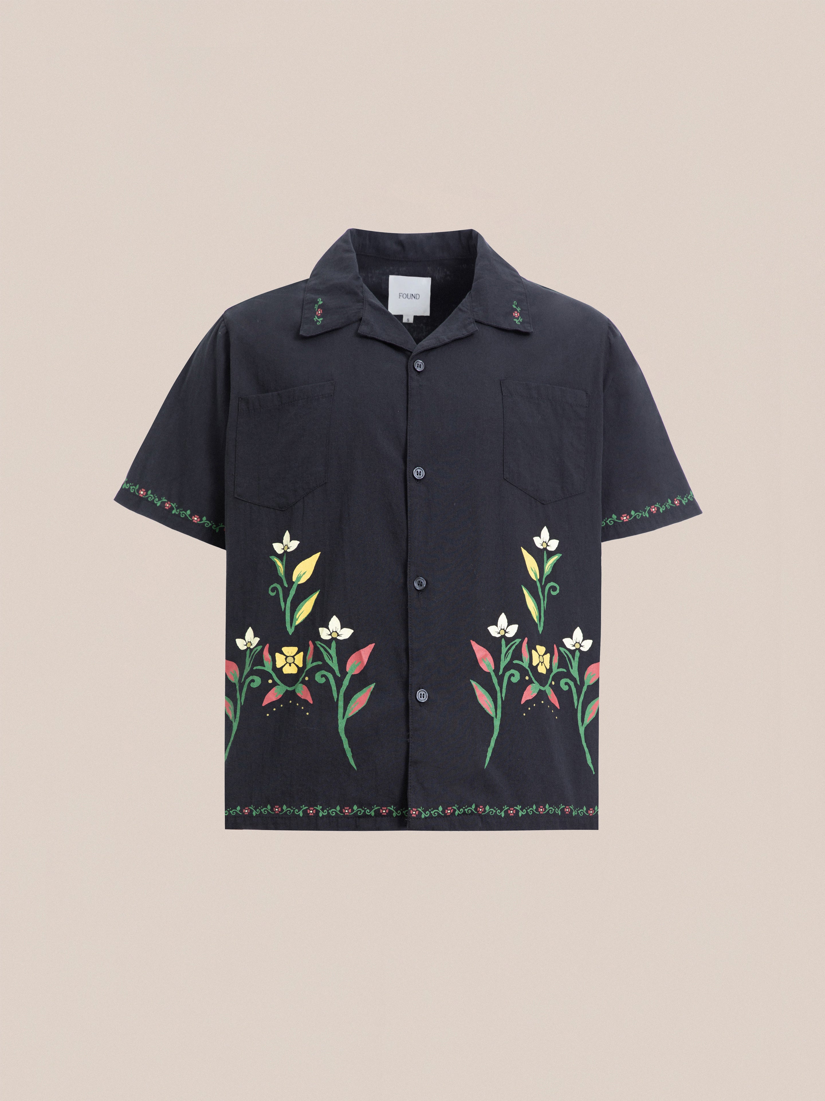 This Profound Floral Camp Shirt features a relaxed fit with short sleeves, a button-up front, and floral designs along the bottom hem and sleeves. Made from 100% cotton, it includes a collar and two chest pockets for added style and convenience.