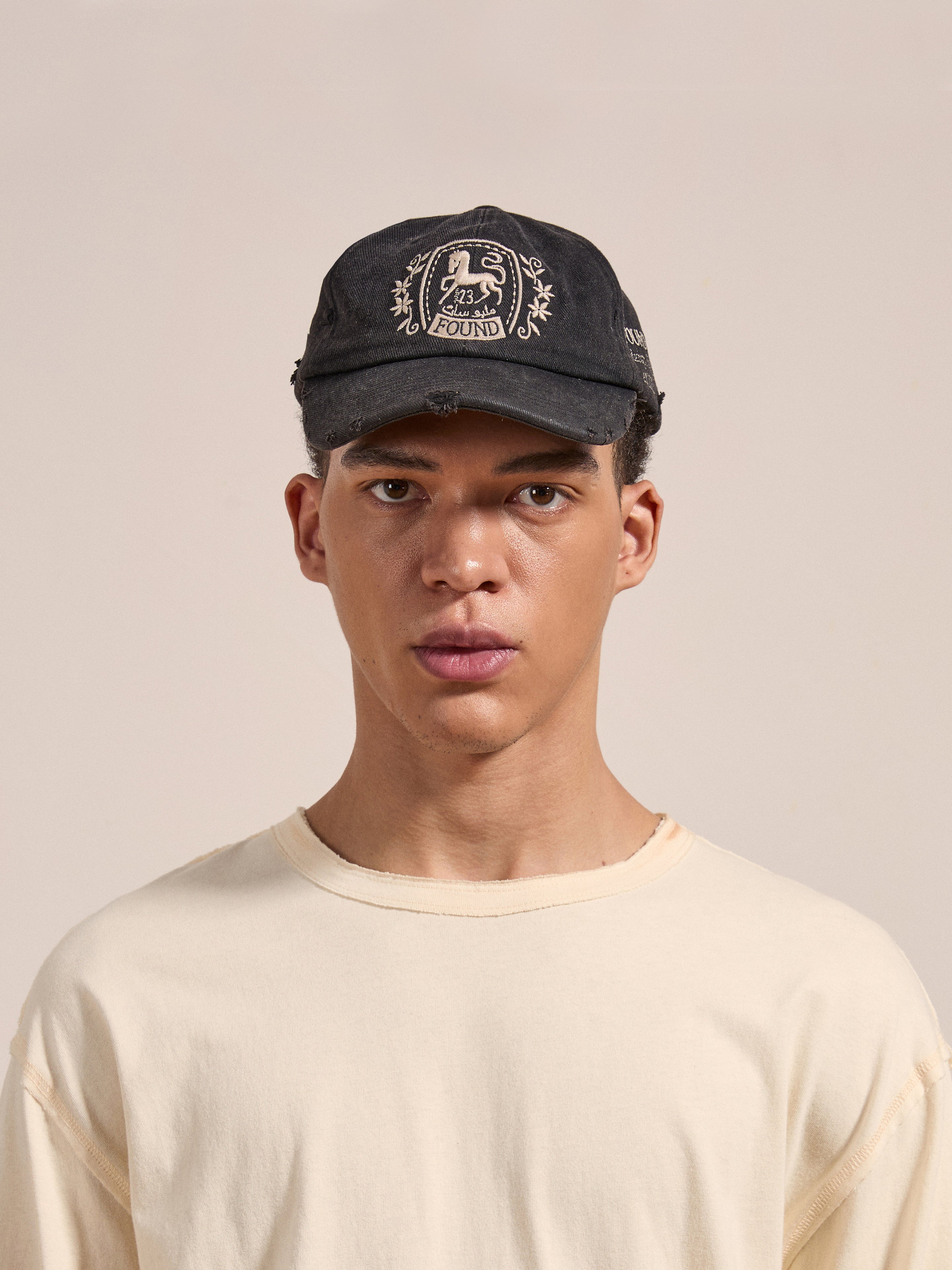 A person wearing a FOUND Logo Crest Cap and a light-colored shirt, standing against a beige background.