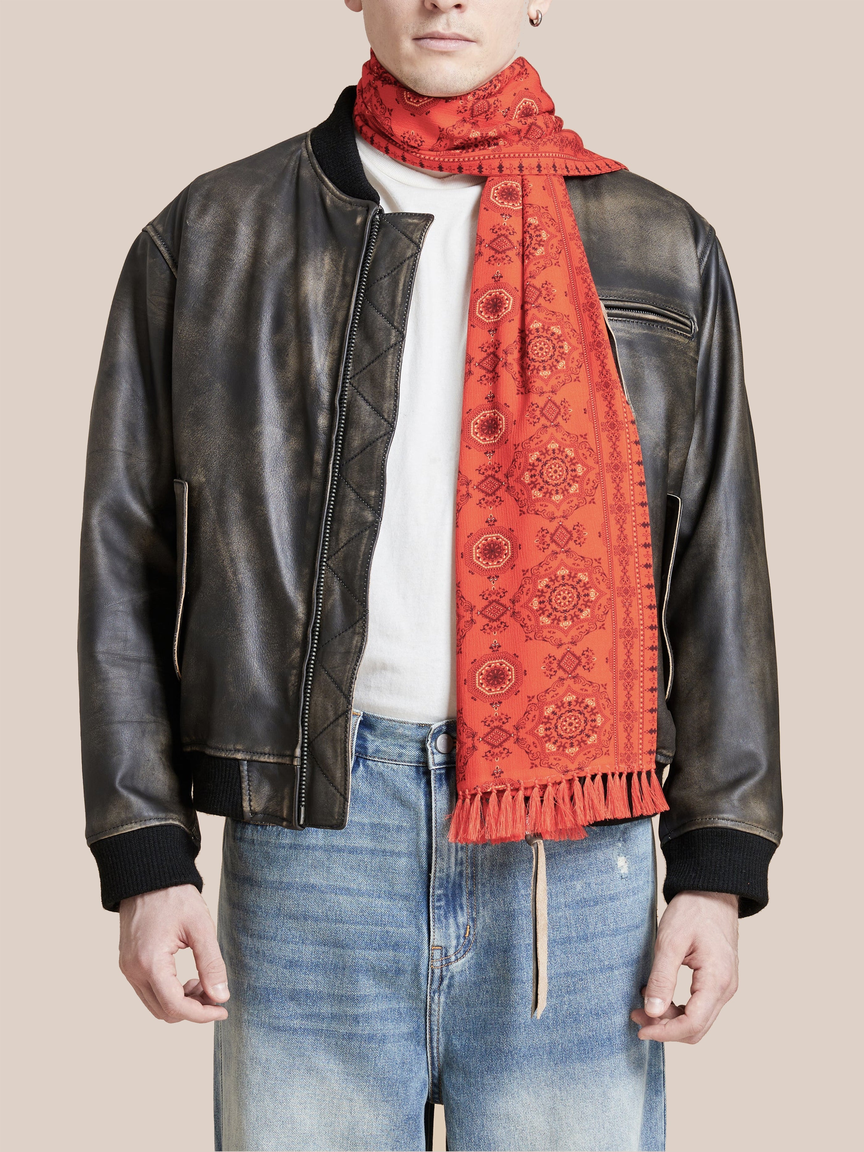 A person wearing a black leather jacket, white shirt, blue jeans, and an orange Grenadine Scarf with hand-tied tassels by Found.