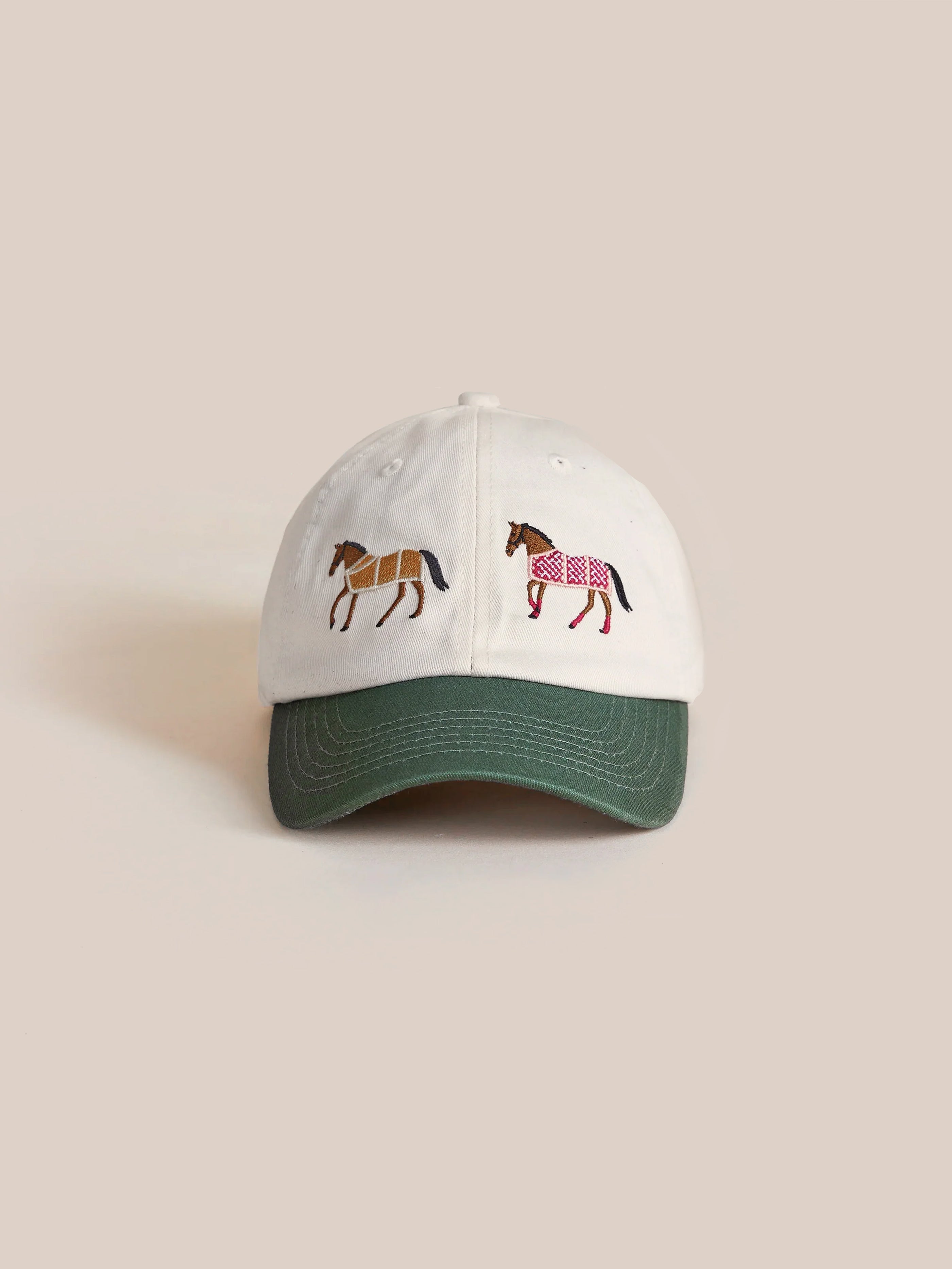 A white Found Horse Equine Cap featuring a green brim and embroidered depictions of two horses on the front, exuding a 70's color-blocking style.