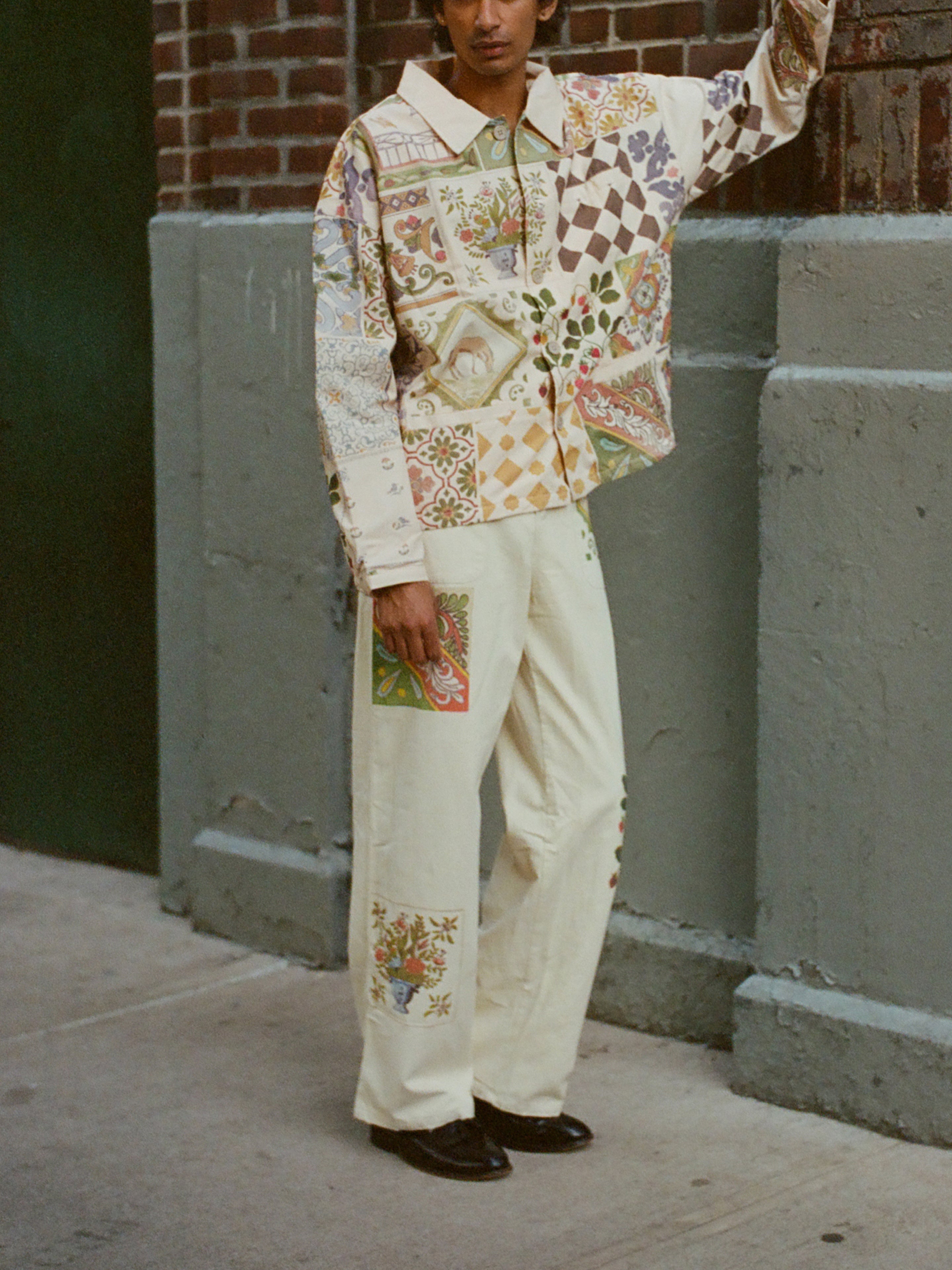 A person wearing Profound's Mosaic Pants and a patterned shirt leans against a brick wall.