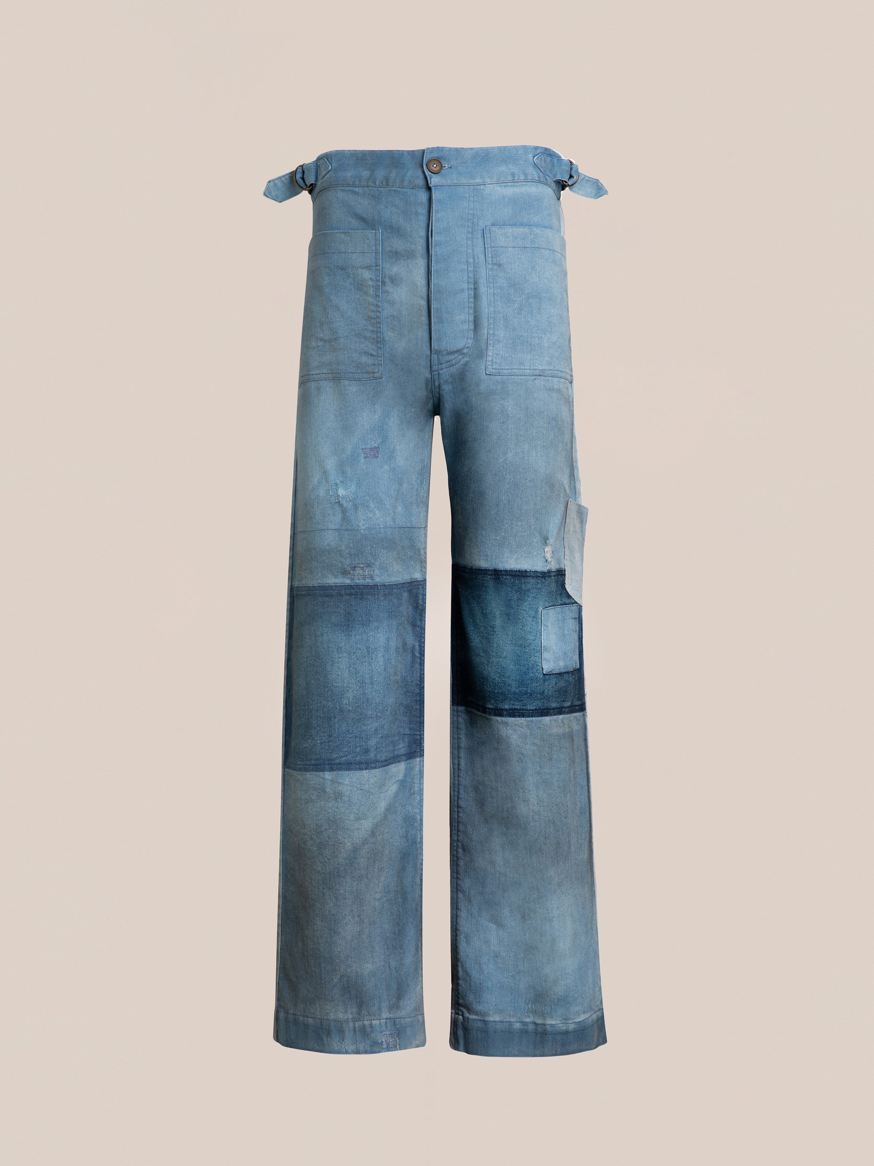 A pair of blue denim jeans with a patchwork design, featuring various shades of blue fabric sewn together, displayed against a plain beige background. These classic slouchy fit Multi Patch Painters Work Pants from FOUND evoke the charm of antique French painter uniforms.