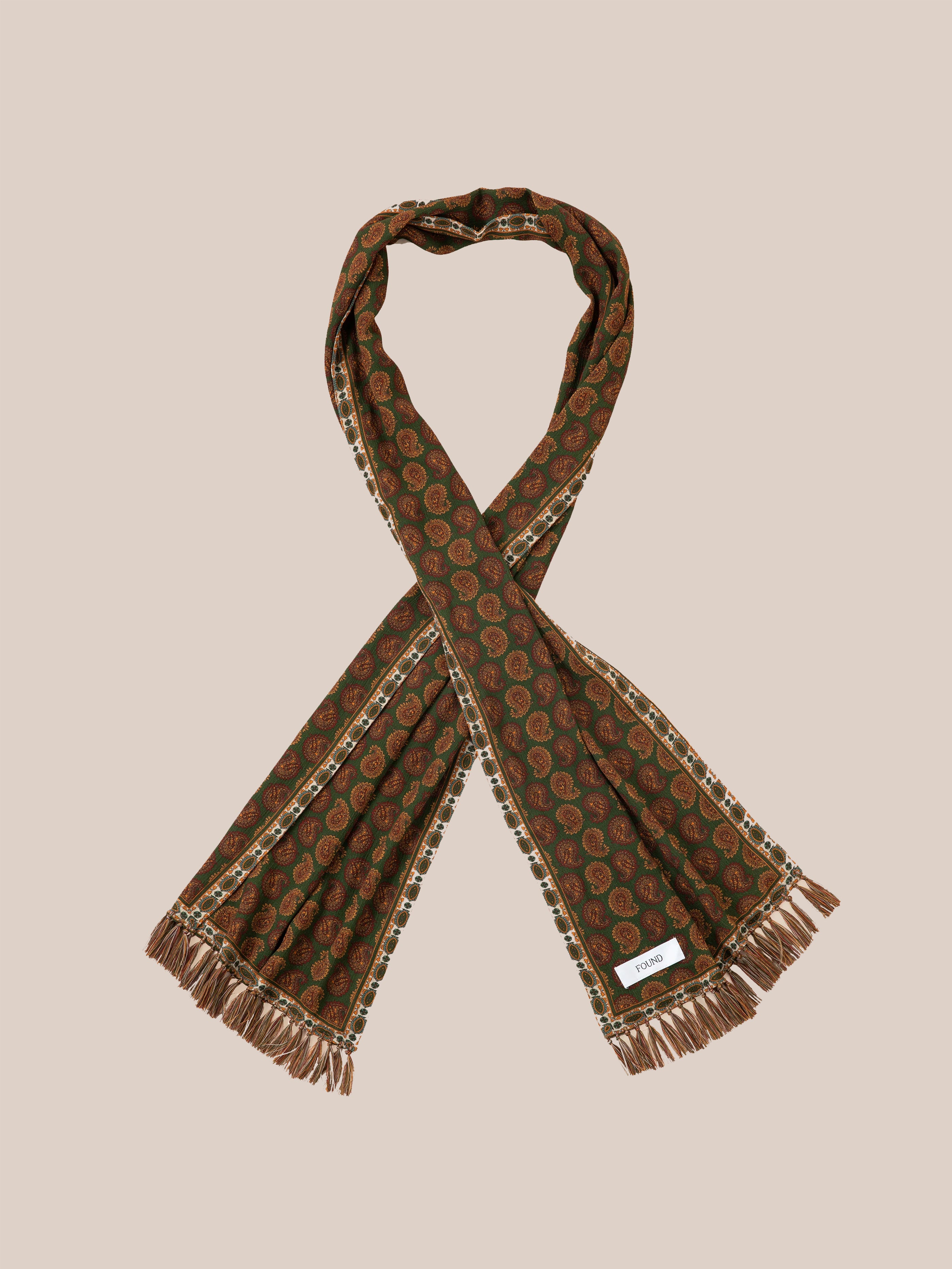 The Paisley Forest Scarf by Found features intricate brown Indo-Aryan prints and fringed edges, elegantly showcased against a plain background. As a versatile accessory, it seamlessly enhances any outfit with its timeless charm.