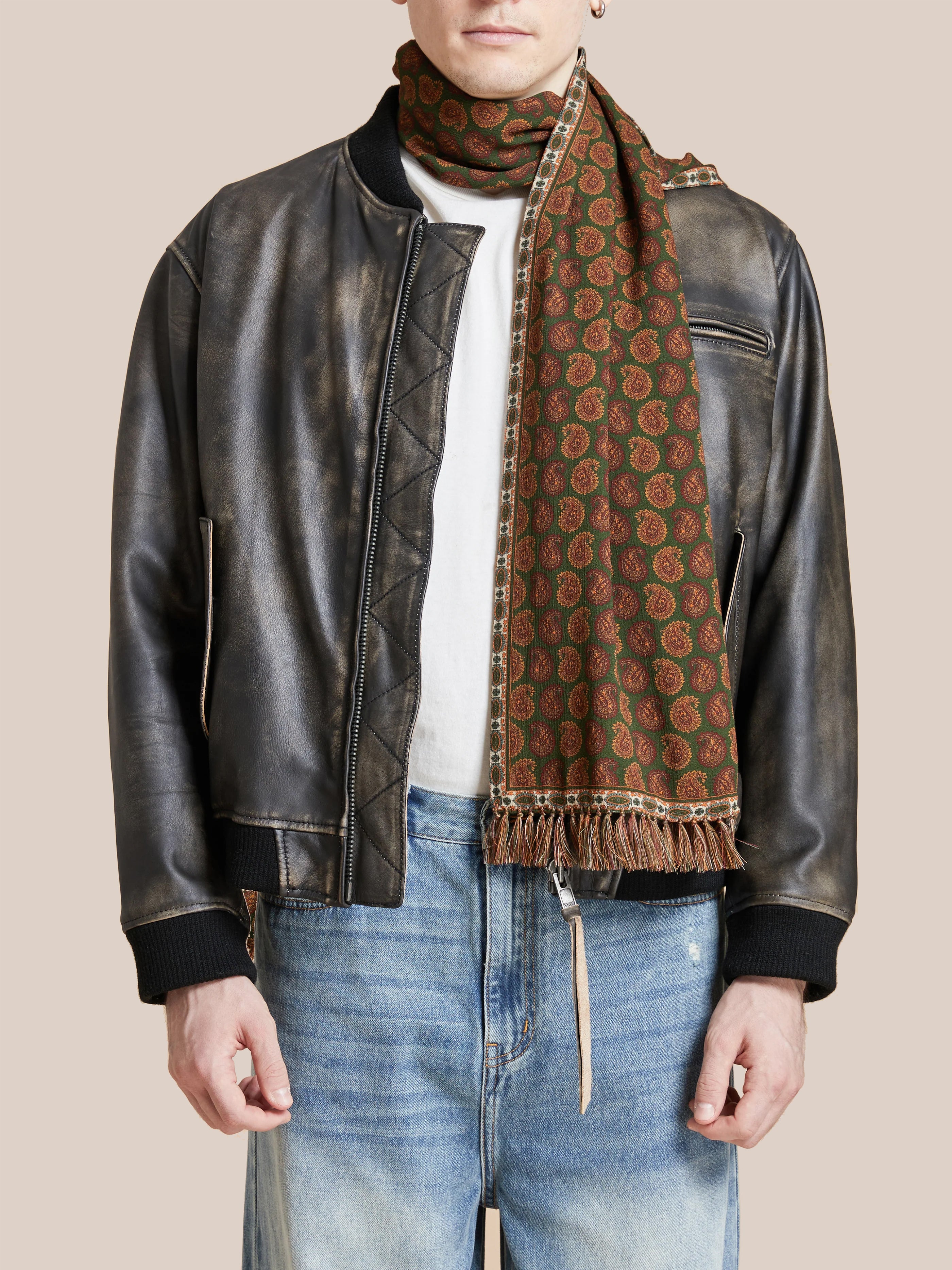 A person wearing a black leather jacket, white shirt, blue jeans, and a Found Paisley Forest Scarf featuring Indo-Aryan prints.