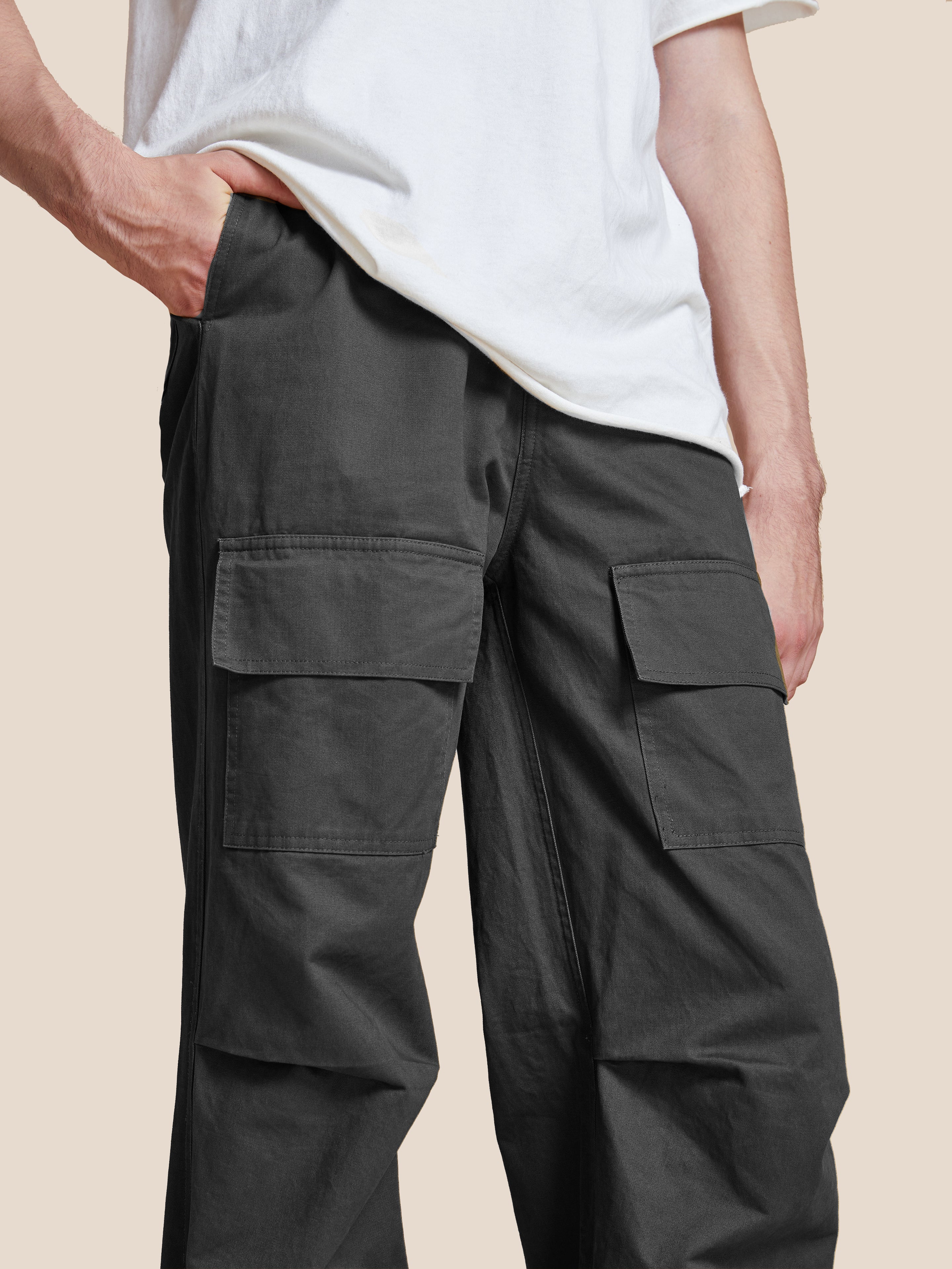 A person wearing a white T-shirt and Found's Parachute Cargo Twill Pants with an adjustable waist stands with one hand in their pocket against a plain background.