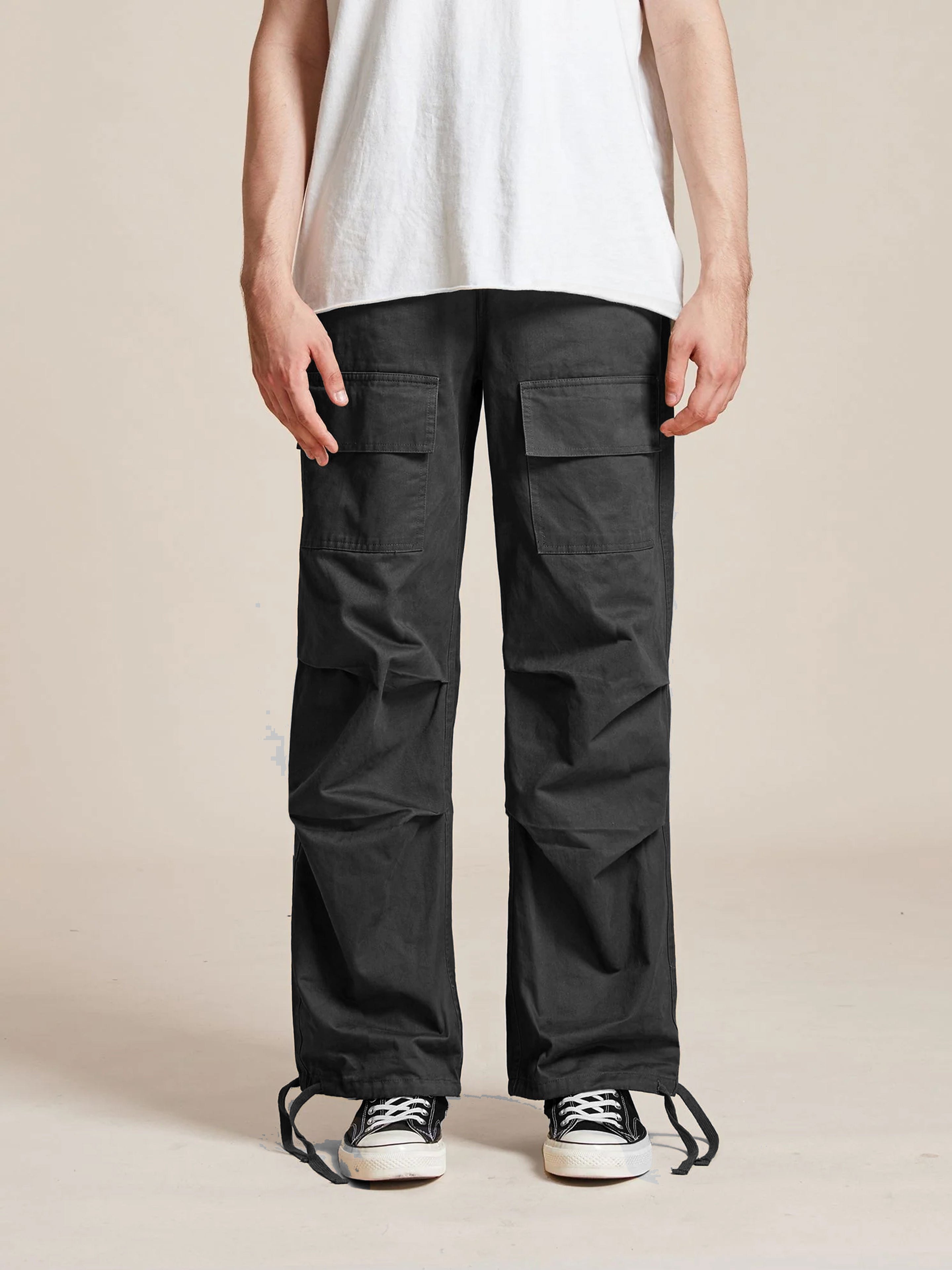 A person wearing a white t-shirt and the Parachute Cargo Twill Pants by Found, which are black wide-leg cargo pants with an adjustable waist, stands against a plain background, paired with black sneakers featuring white soles.