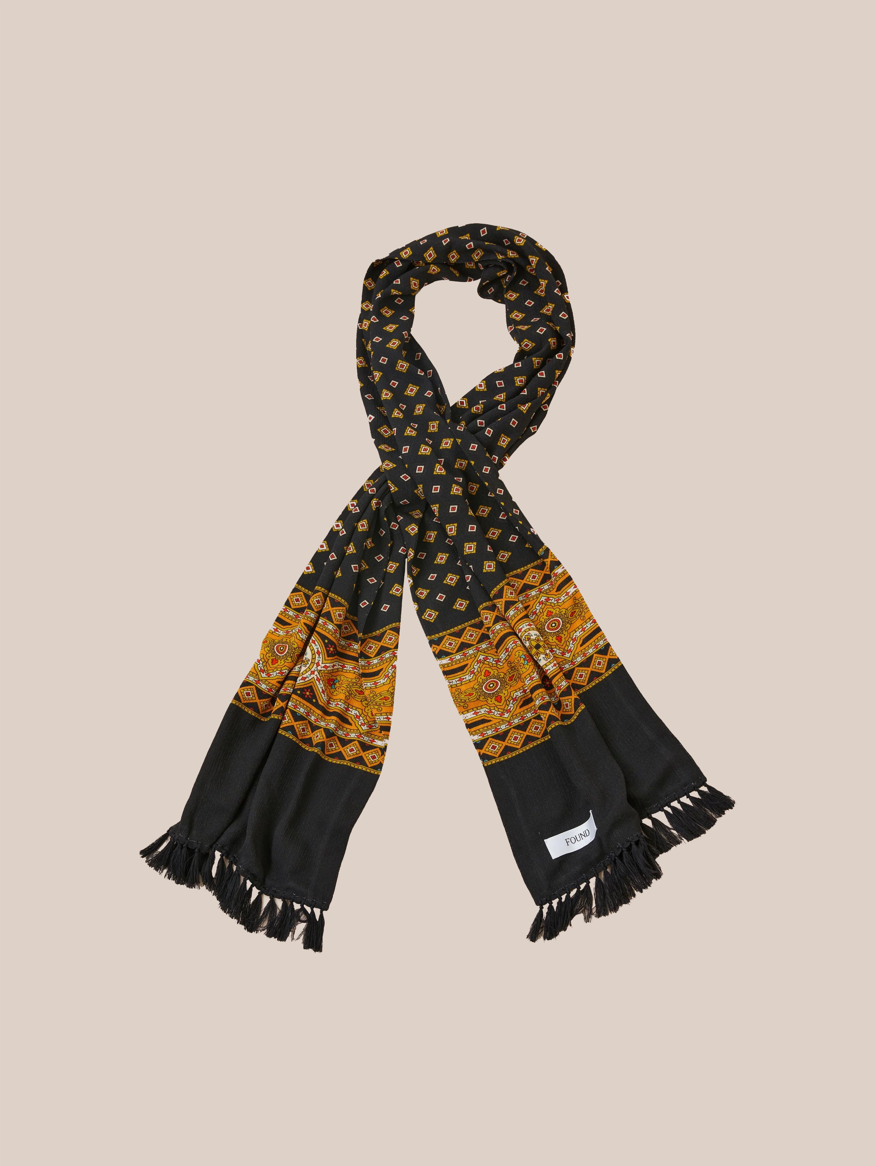 The Found Pastures Print Scarf showcases a striking black and orange pattern, gracefully looping with hand-tied tassels adorning the ends.