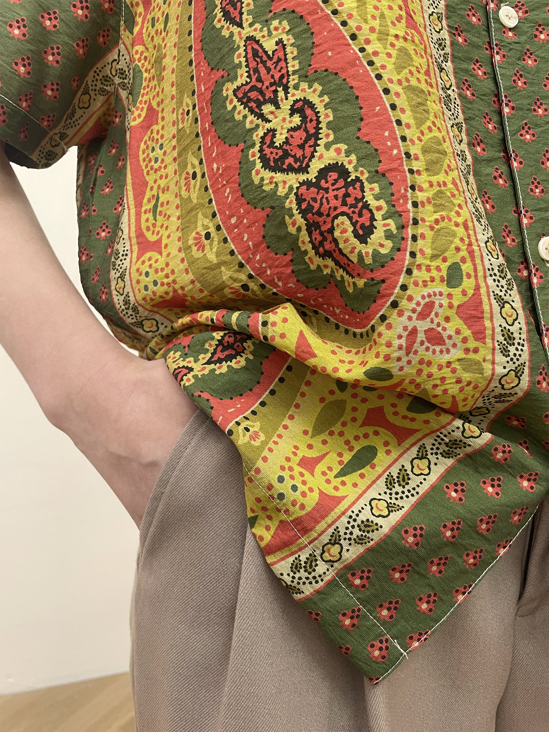 Close-up of a person wearing a colorful Found Pench Paisley SS Camp Shirt with one hand in the pocket of beige pants.