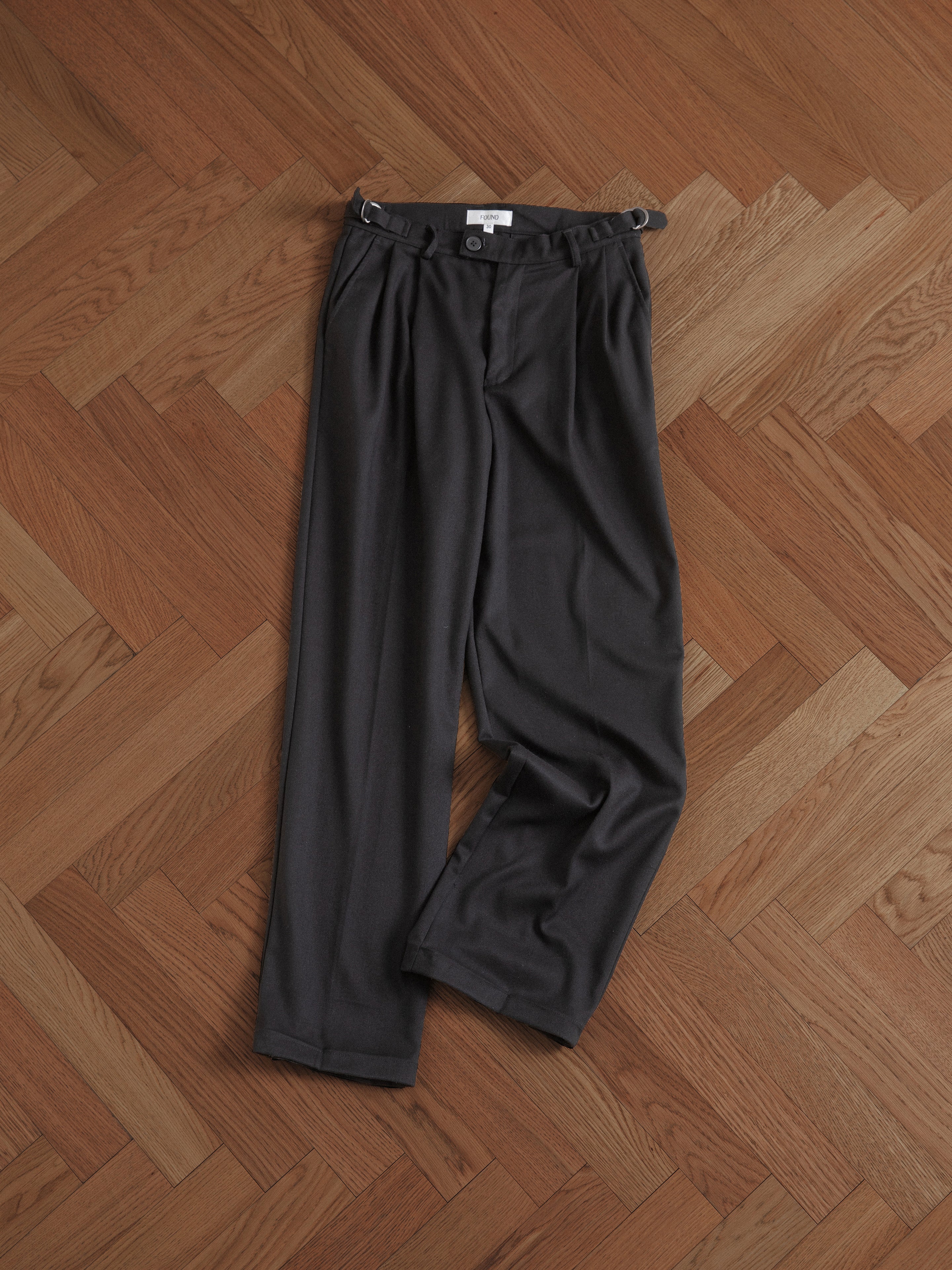 A pair of Found pleated trousers on a wooden floor.