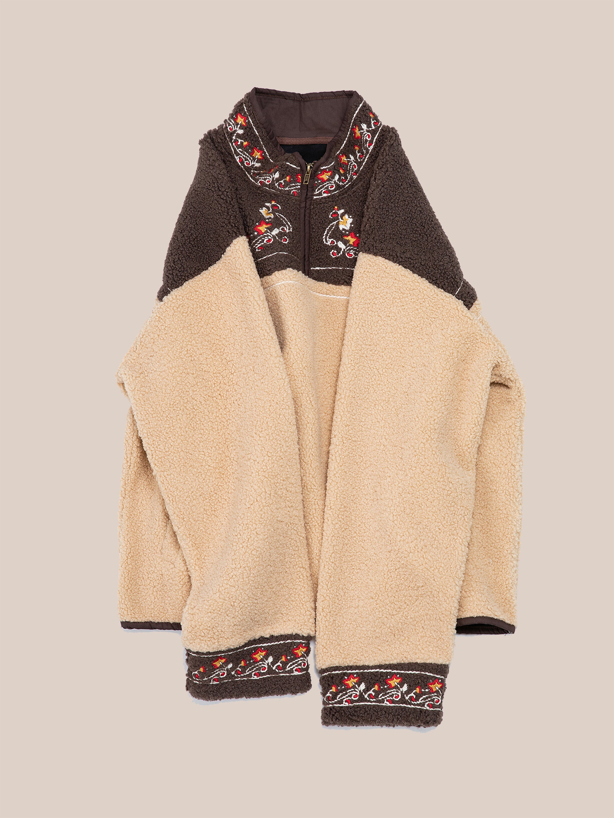 The Pahari Floral Embroidered Sherpa Pullover by FOUND, featuring beige and brown shades, showcases intricate floral embroidery on the collar, cuffs, and hem as it rests against a neutral background.