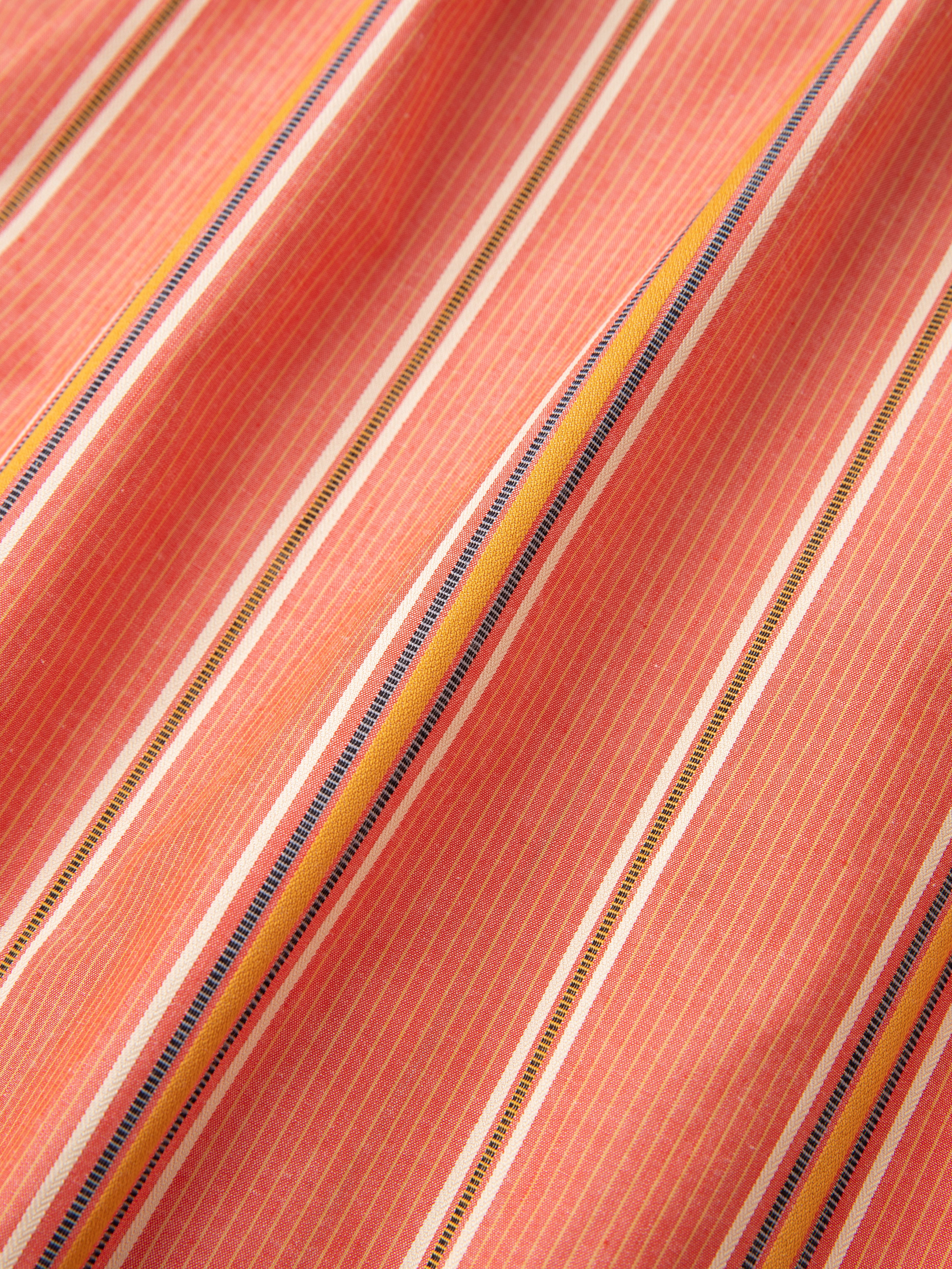 Close-up of a Found Stripe Citrus LS Camp Shirt fabric with pink and white pinstripes and multicolored horizontal stripes in yellow, blue, and white. The material appears to have a slightly textured surface.