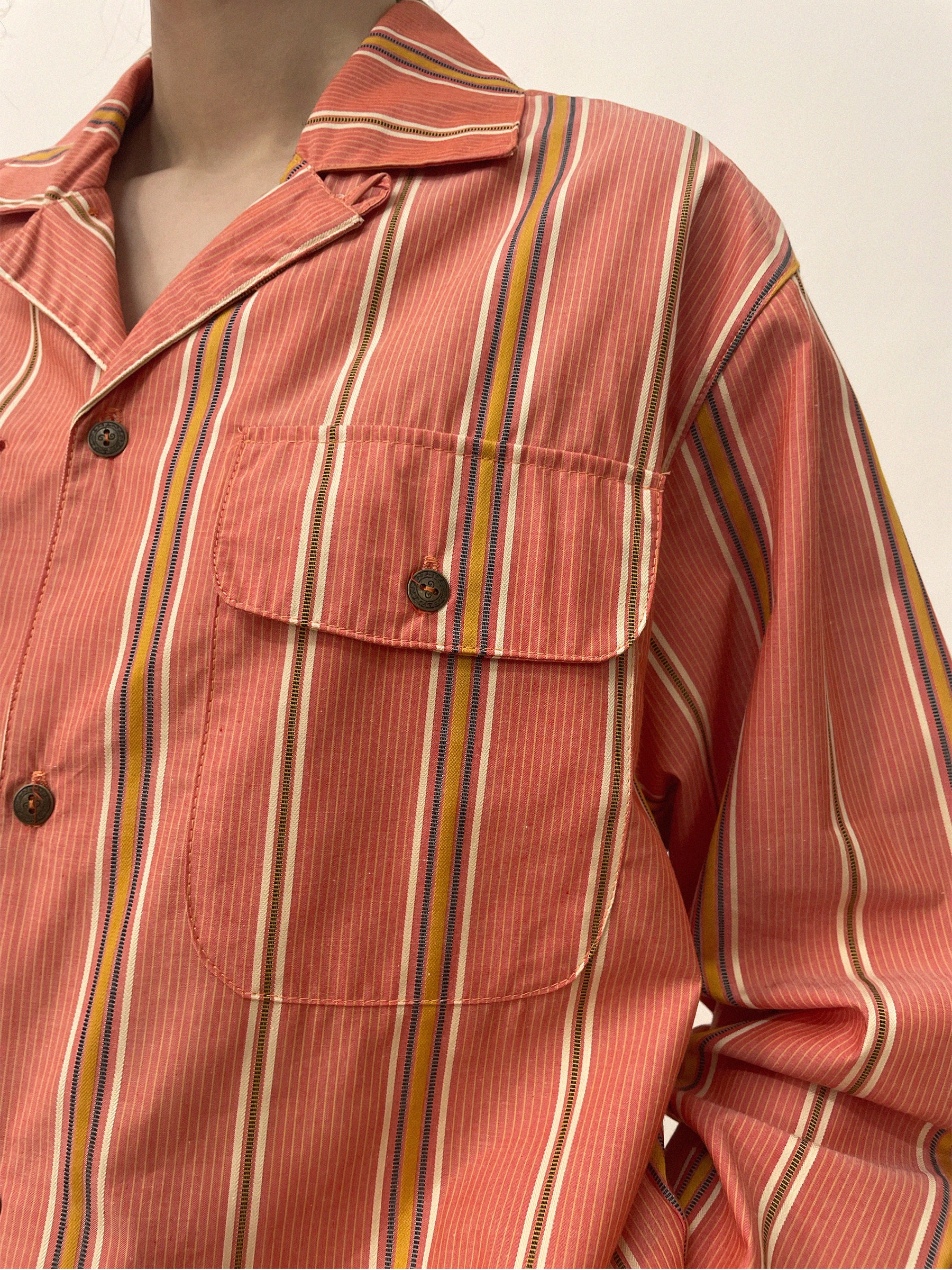 Close-up of a person wearing a Found Stripe Citrus LS Camp Shirt with red, white, and yellow vertical stripes. The shirt features dual chest pockets and a front button closure.