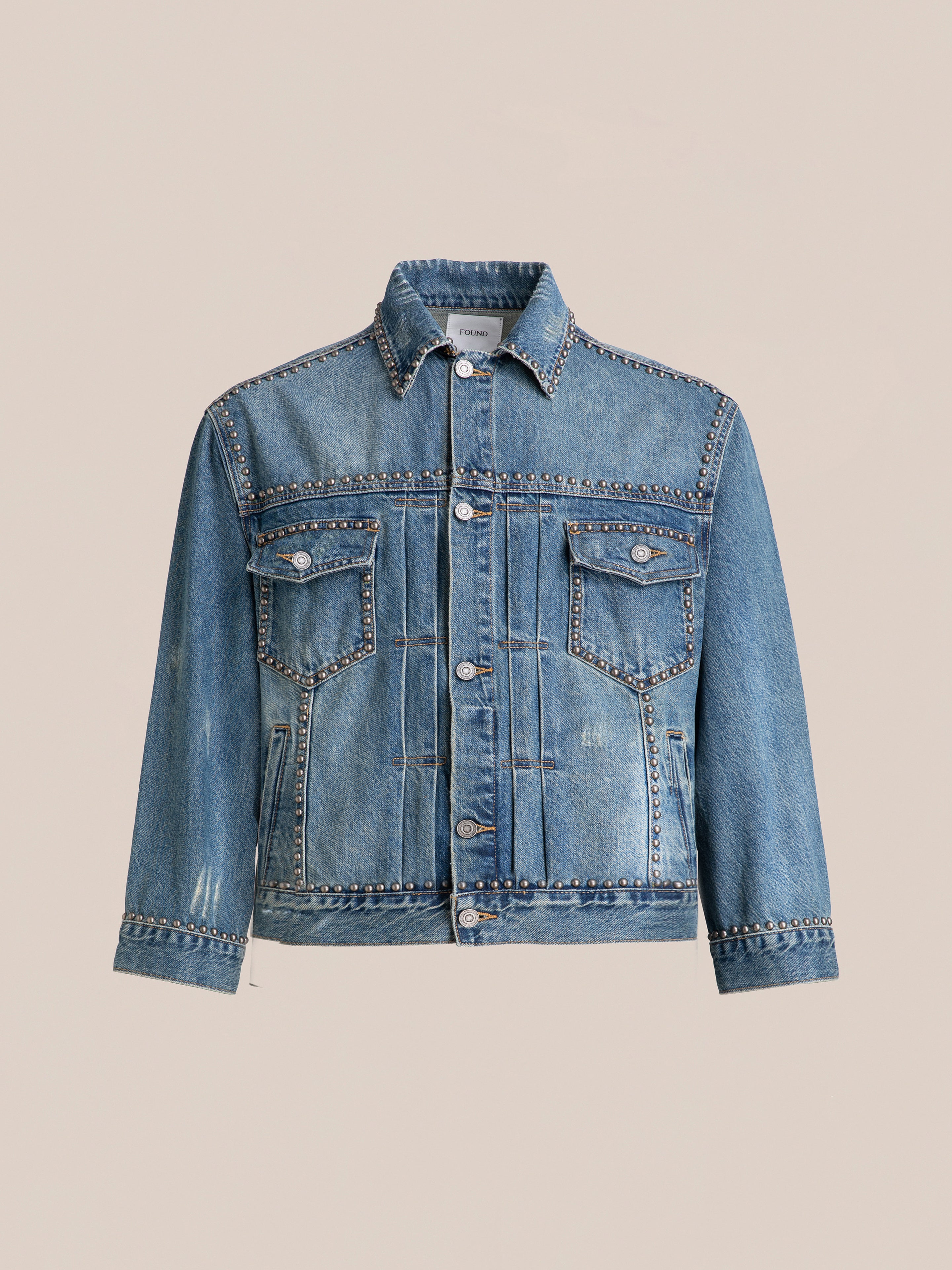 The FOUND Azar Studded Denim Trucker Jacket in vintage blue wash flaunts an oversized boxy fit, complete with metal stud detailing on the collar, pockets, and seams. This blue denim jacket showcases buttons down the front, two chest pockets with flaps, and a slightly distressed finish.