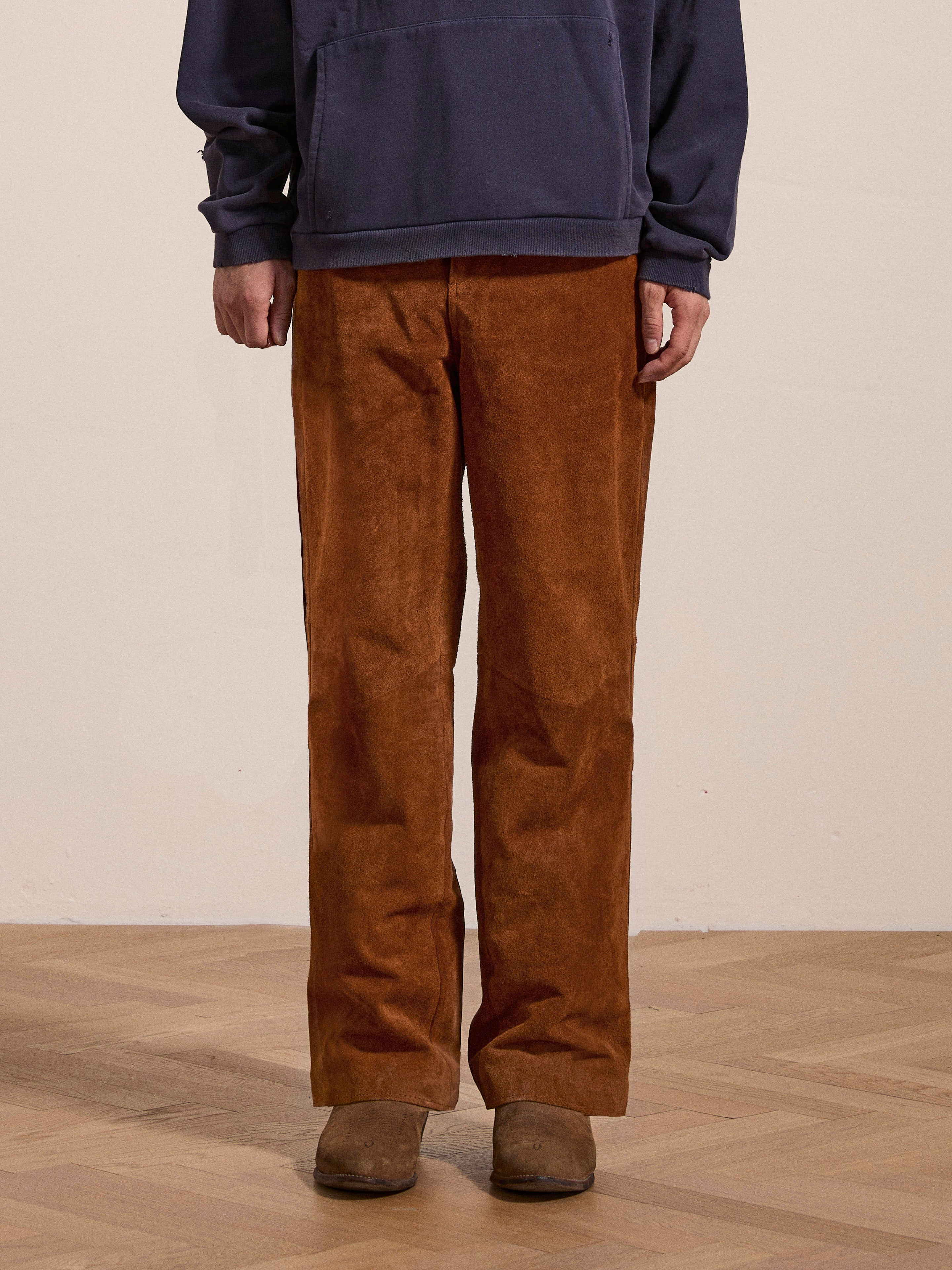 A person wearing ethically sourced materials, including FOUND's Suede Moto Pants and a dark blue sweatshirt, is standing on a wooden floor. Only their lower legs and torso are visible.