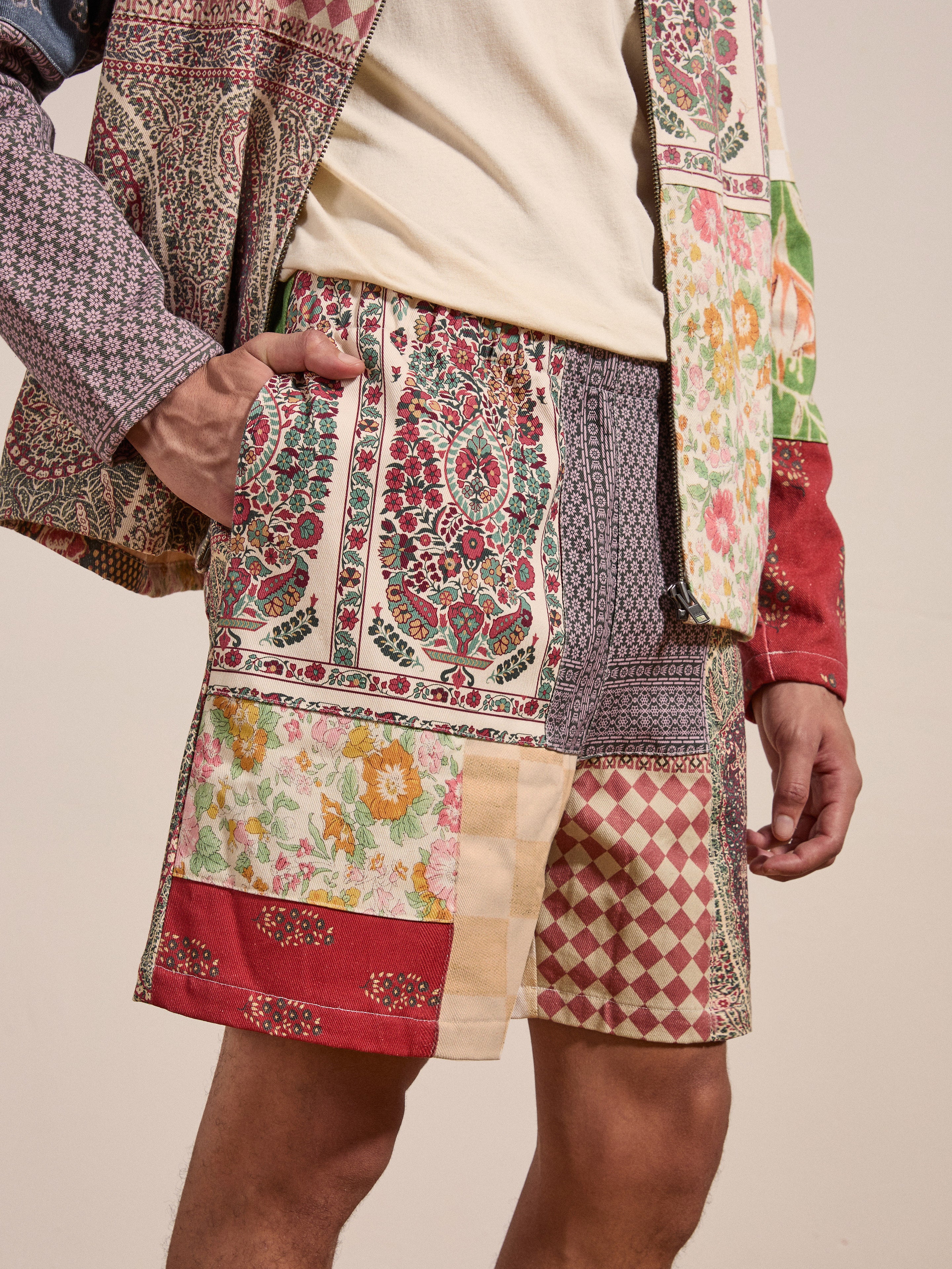 A person is wearing the Tapestry Twill Shorts and a matching jacket by FOUND, showcasing a mixed-pattern outfit that features an array of floral and geometric designs. They have one hand casually placed in a pocket.