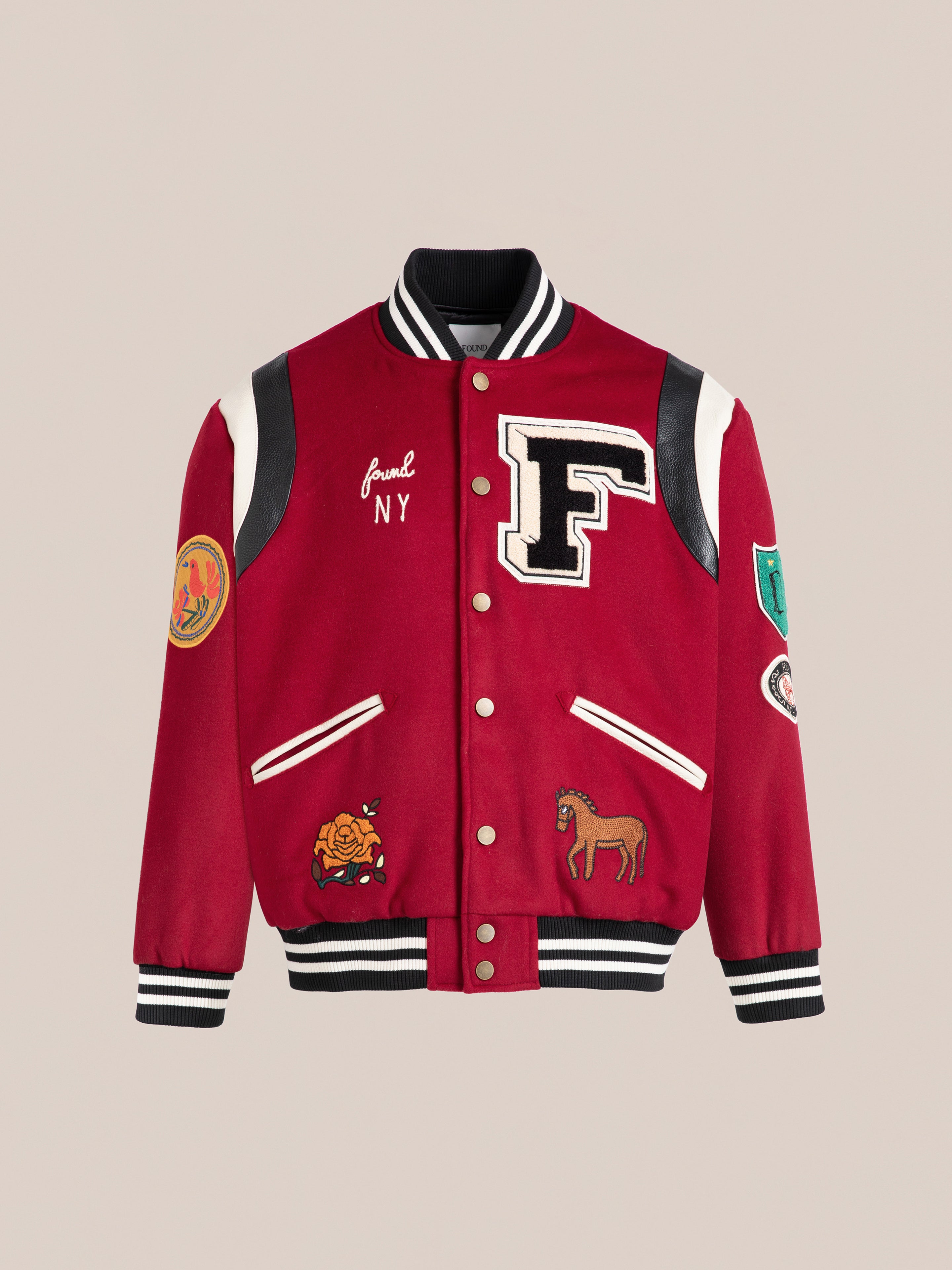 The red Letterman Varsity Jacket by FOUND features a wool blend body with black and white trim. It includes patches like a large "F," rose, horse, "NY" text, and a chenille chest logo.