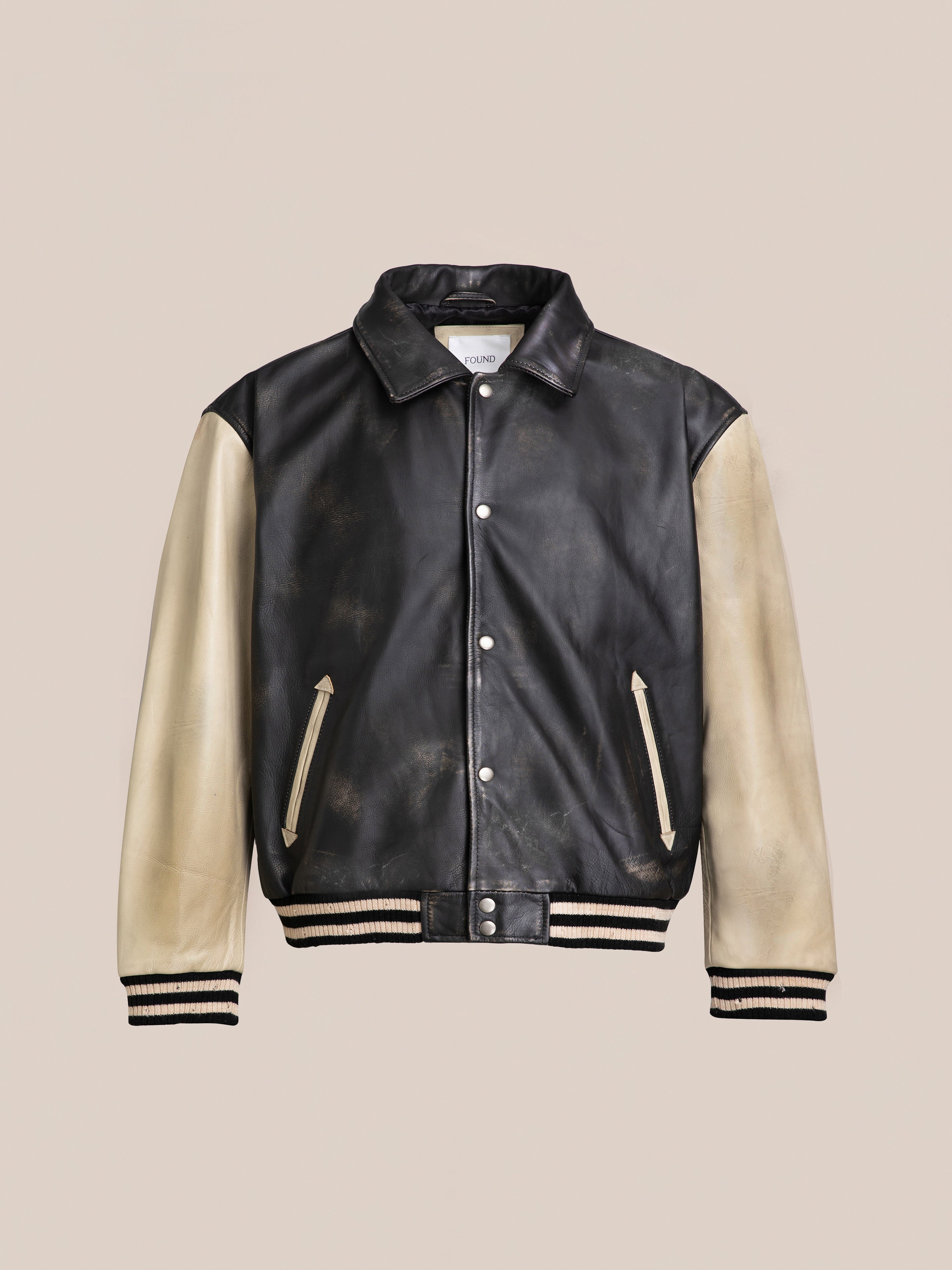 The FOUND Logan Distressed Leather Varsity Jacket showcases a striking black and beige design made from genuine hand-distressed leather, complete with a button-up front, along with ribbed cuffs and hem. For added comfort, the jacket features a luxurious satin lining.