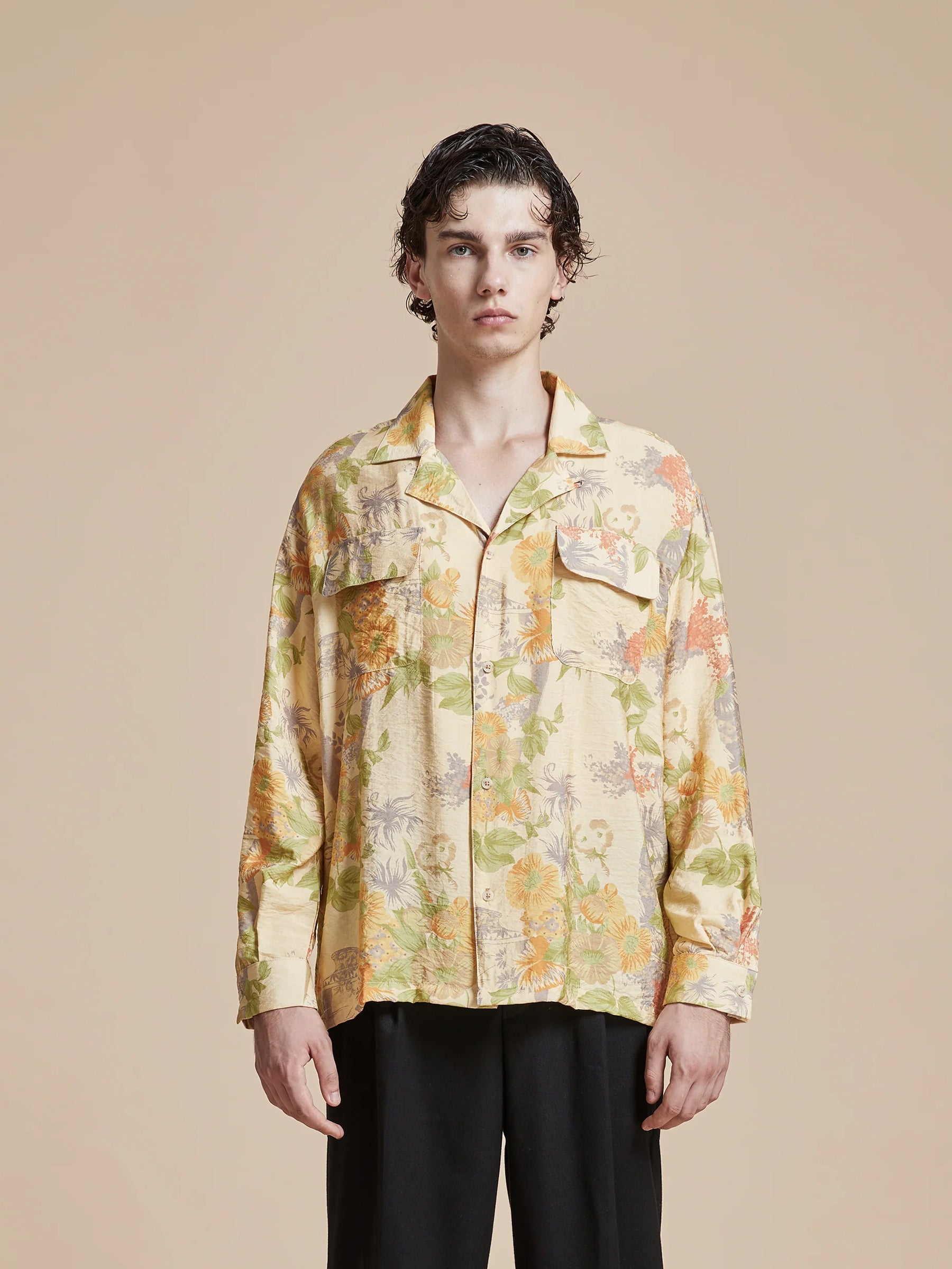 A model wearing a yellow floral shirt with Phulkari motifs, the Found Meraj Vase Pot Long Sleeve Camp Shirt, and black pants.