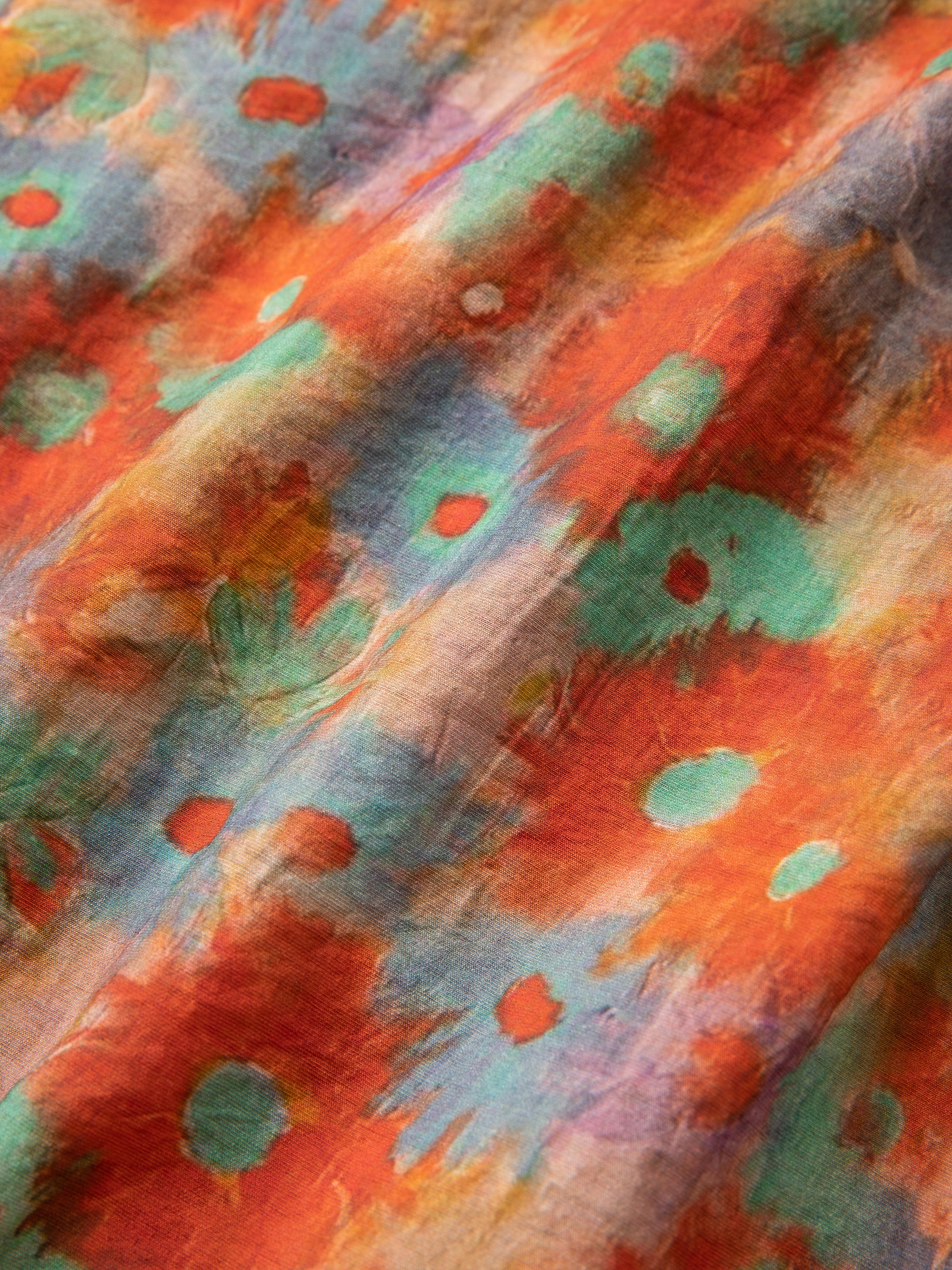 Close-up of a colorful Waterblend LS Camp Shirt by Found with a vibrant pattern featuring abstract shapes in hues of orange, red, teal, and green. The texture appears soft and slightly wrinkled, accentuating the shirt's dual chest pockets.